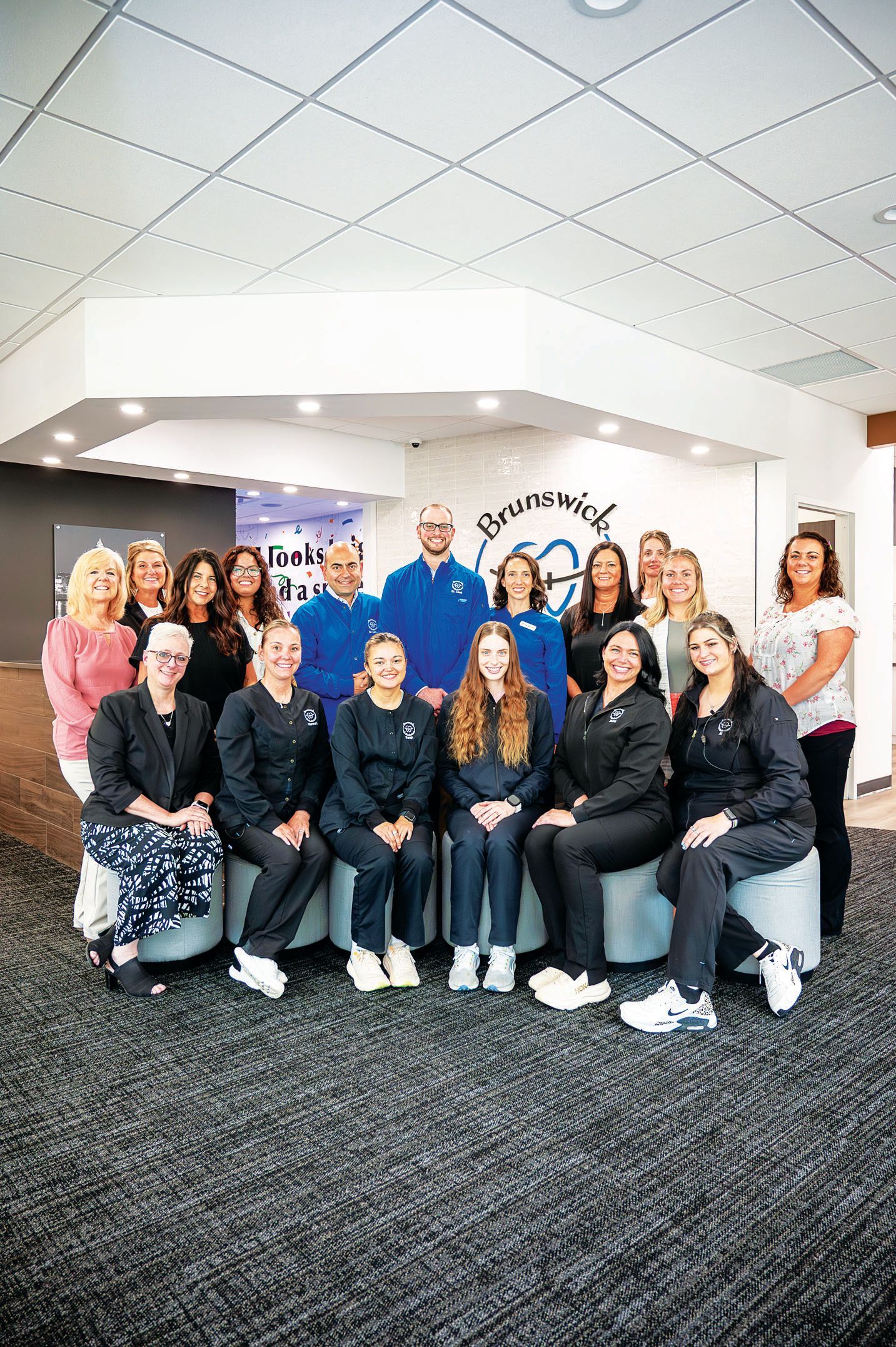 A diverse group of staff members in professional attire and scrubs posing together in a brightly lit modern office lobby.