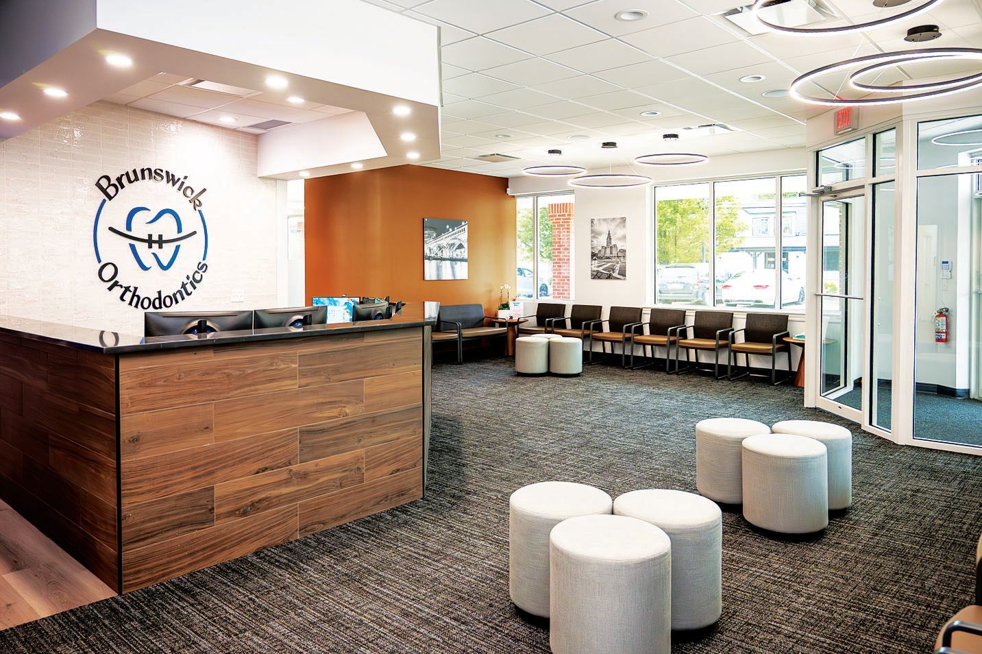 Modern orthodontist office reception area with a wood-paneled desk, logo on the wall, and seating in a bright lobby.