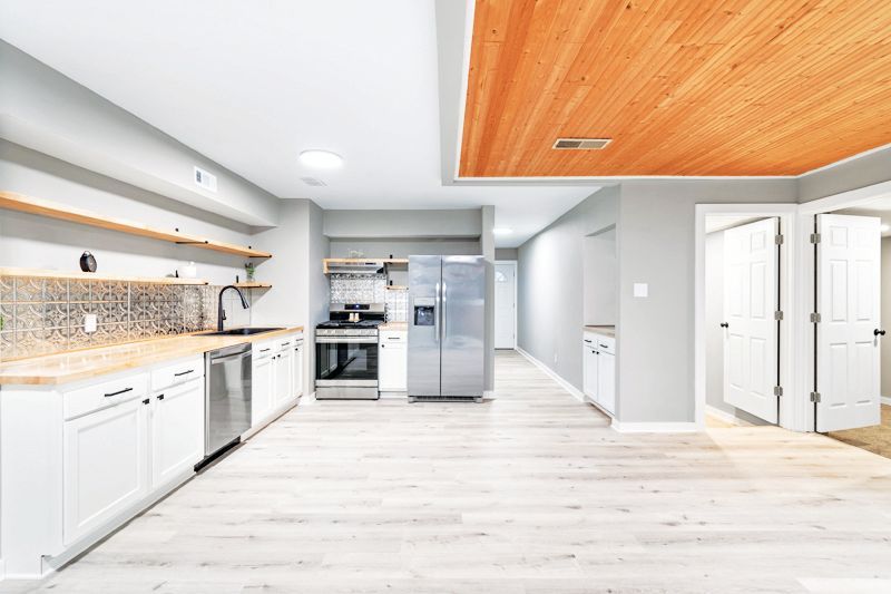 A modern kitchen with white cabinets, light wood open shelves, stainless steel appliances, and a wood-paneled ceiling.