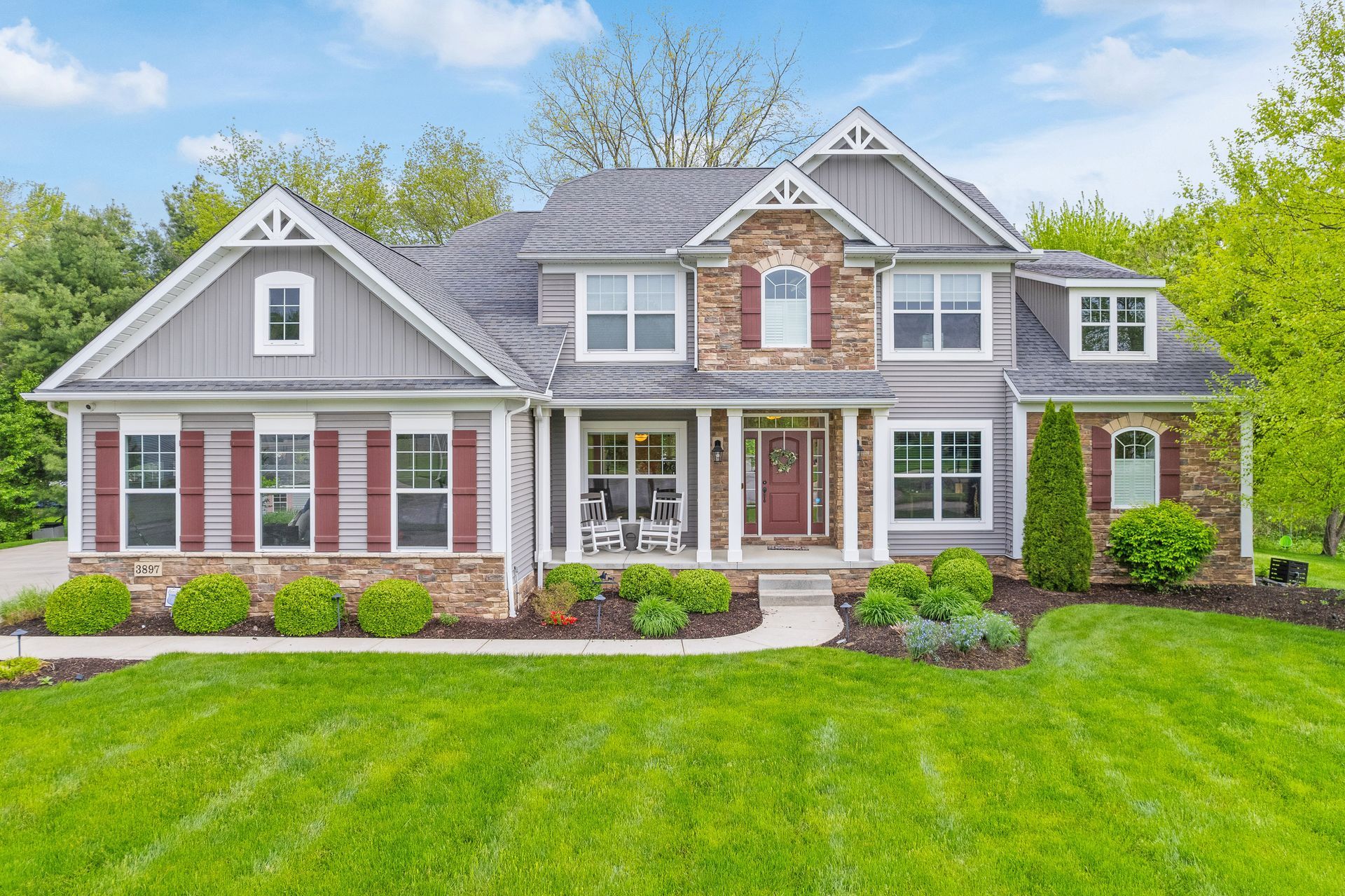A two-story suburban home with gray siding, stone accents, brown shutters, and a well-manicured green lawn.