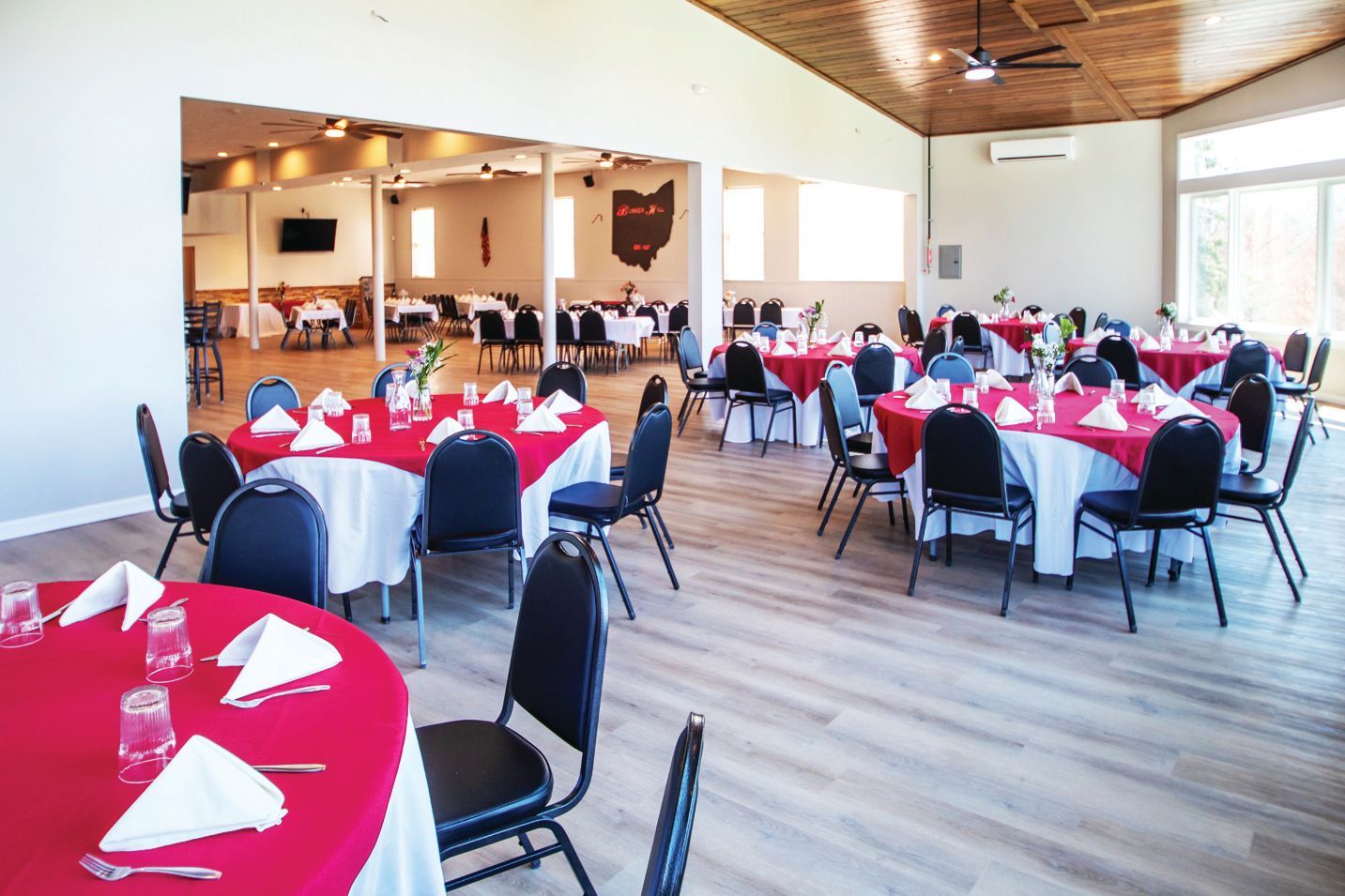 Event space with round tables covered in red tablecloths and white napkins set for a formal gathering.
