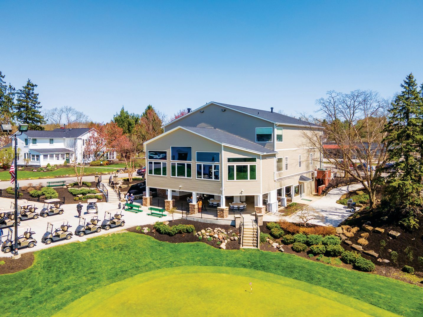 A multi-story beige golf clubhouse with a green lawn in the foreground and a line of parked golf carts to the left.