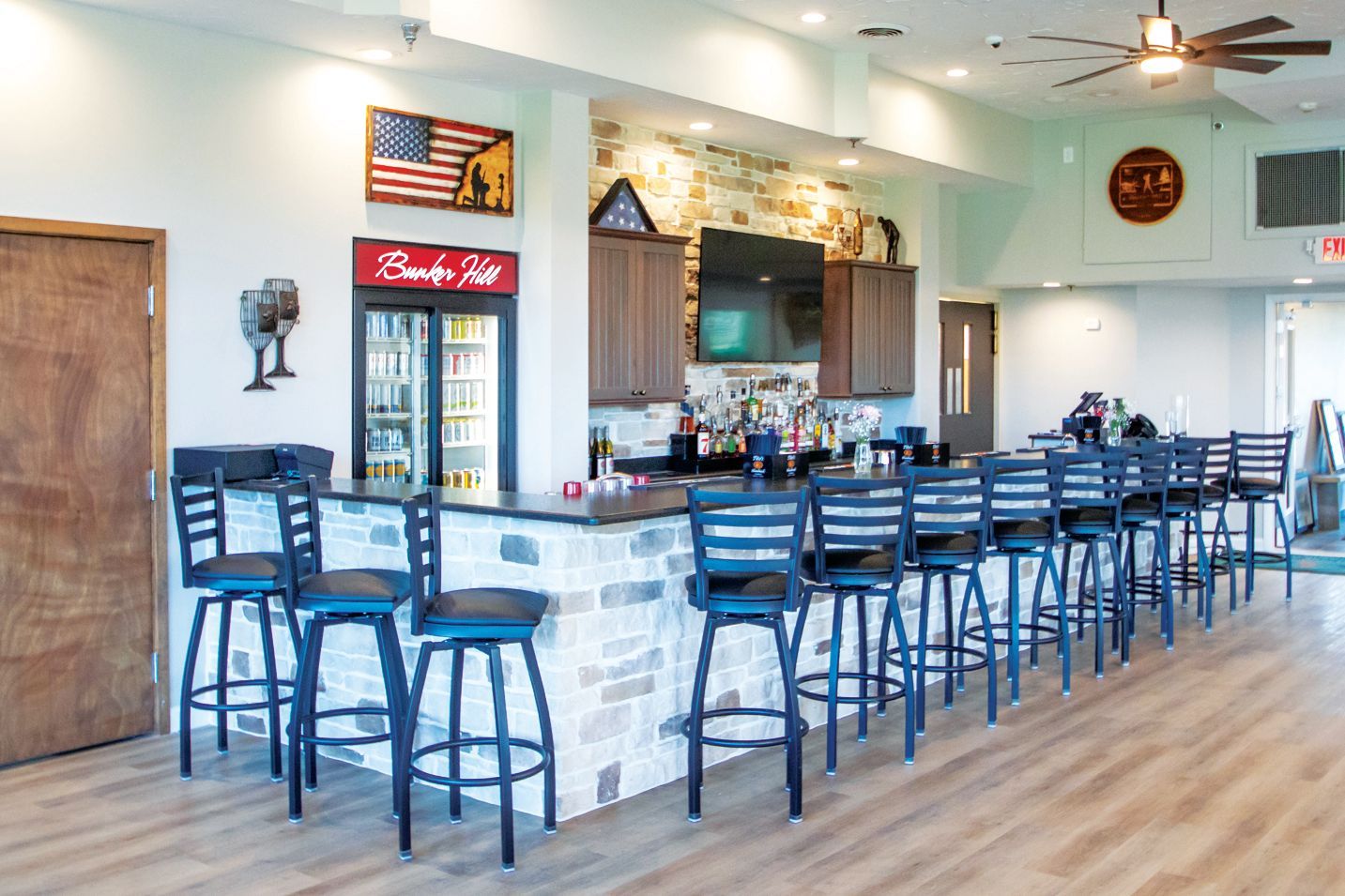 A modern bar with a stone counter, several dark blue bar stools, wood cabinets, and a glass-front beverage refrigerator.