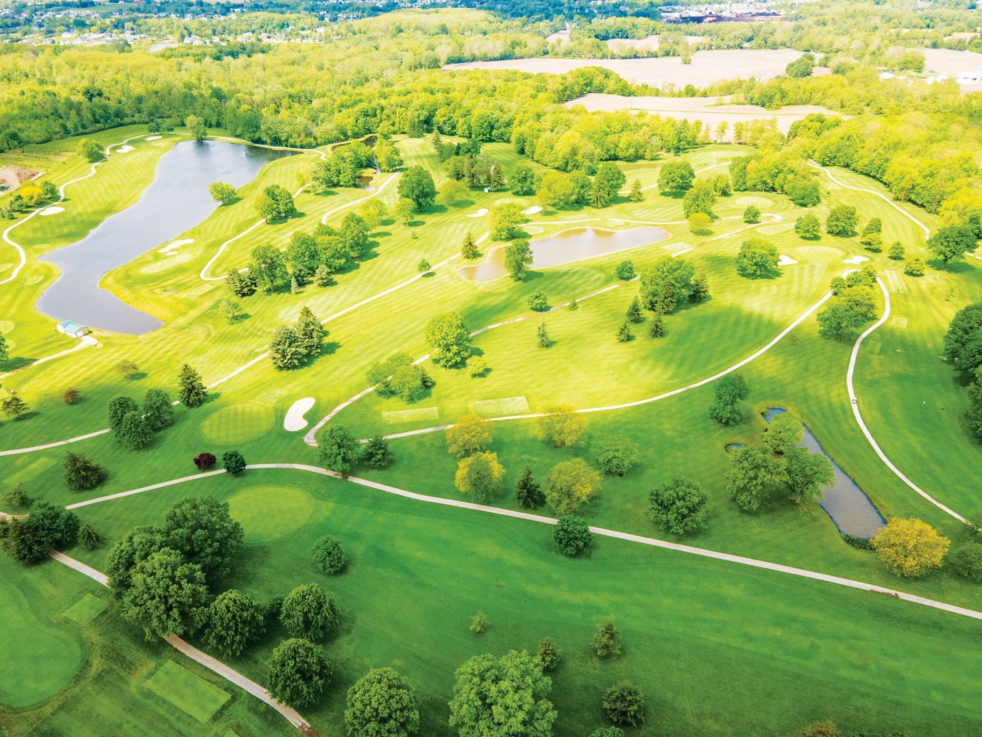 Aerial view of a lush green golf course featuring tree-lined fairways, sand traps, and small ponds under bright sunlight.