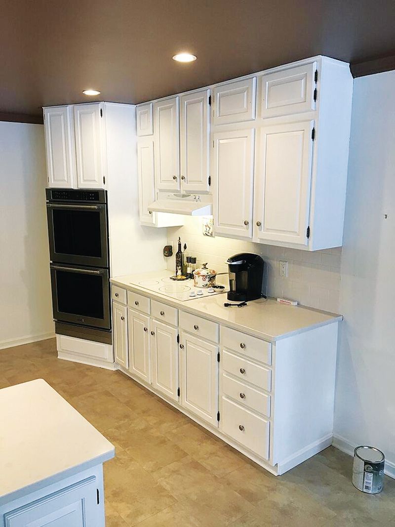 White kitchen cabinets with a built-in double oven and light-colored countertops against a dark ceiling.