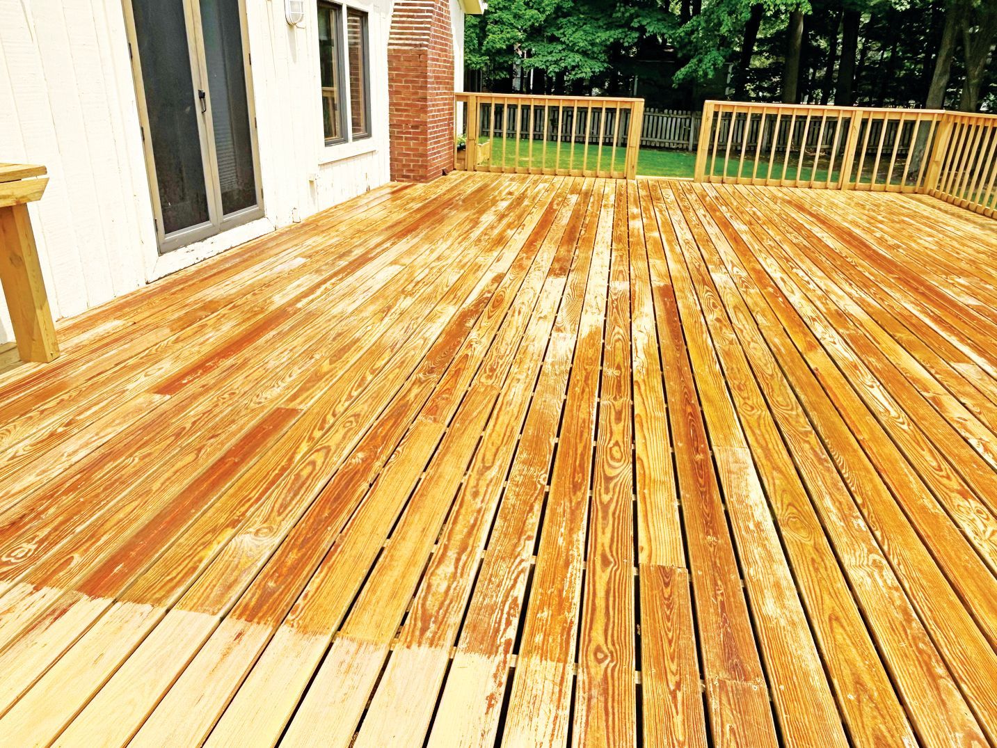 A wooden deck undergoing partial staining, showing a contrast between lighter untreated wood and richer, stained planks.