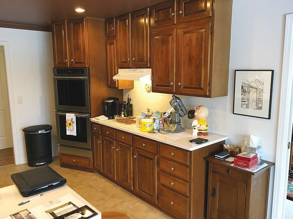 Kitchen with warm-toned wooden cabinets, white countertops, double wall oven, and a small side cabinet on a light floor.