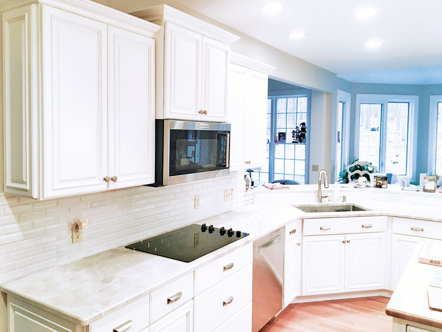A bright kitchen with white shaker-style cabinets, stainless steel appliances, a glass stovetop, and marble countertops.