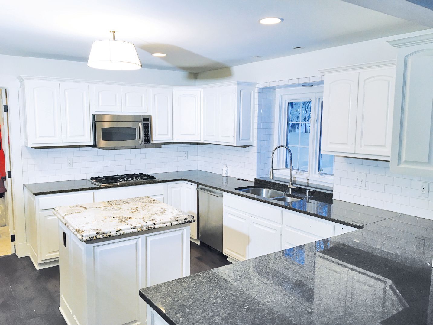A modern kitchen with white cabinets, dark granite countertops, stainless steel appliances, and a central island.