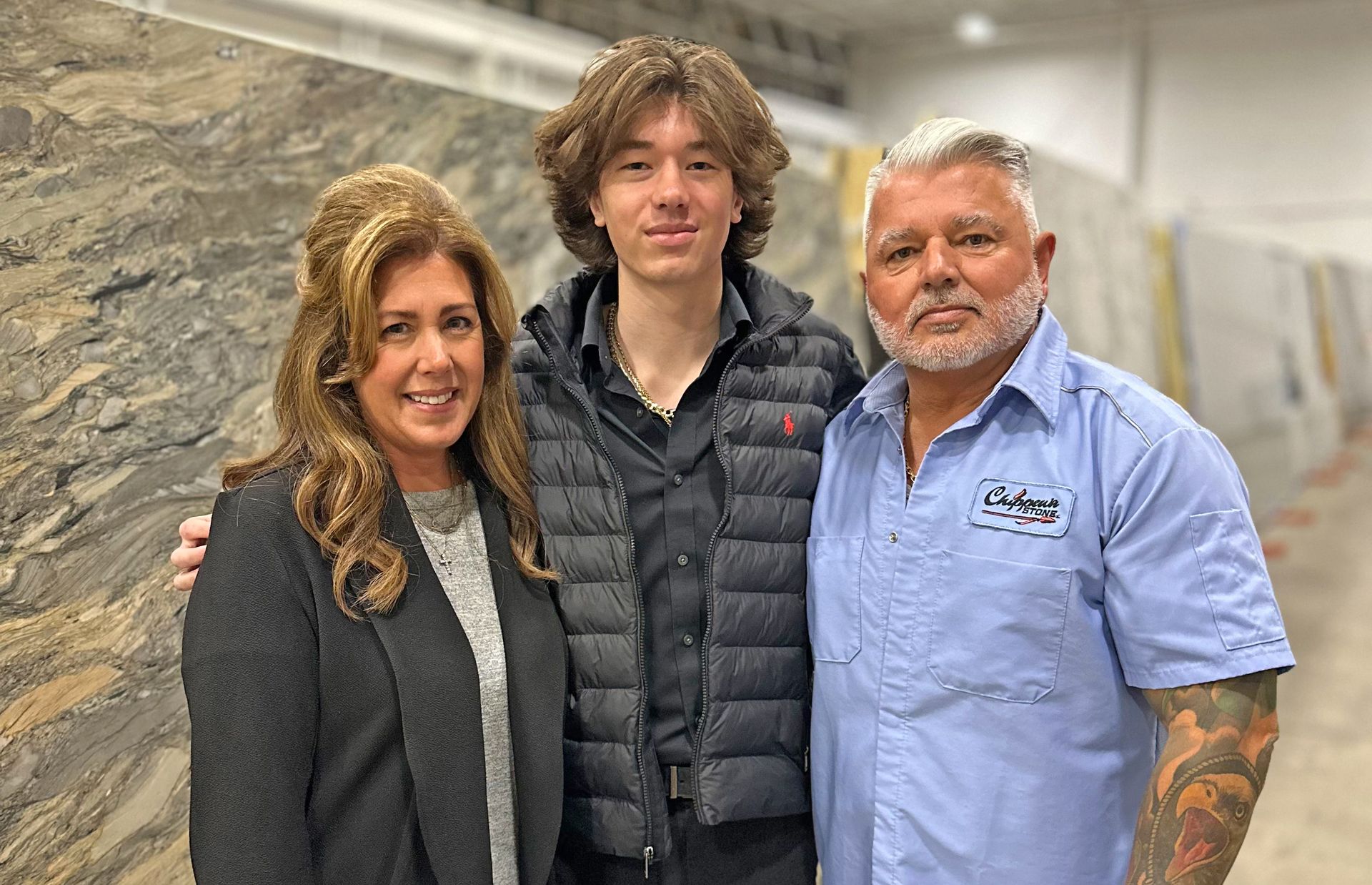 Three people stand smiling for a photo in a showroom filled with large stone slabs.
