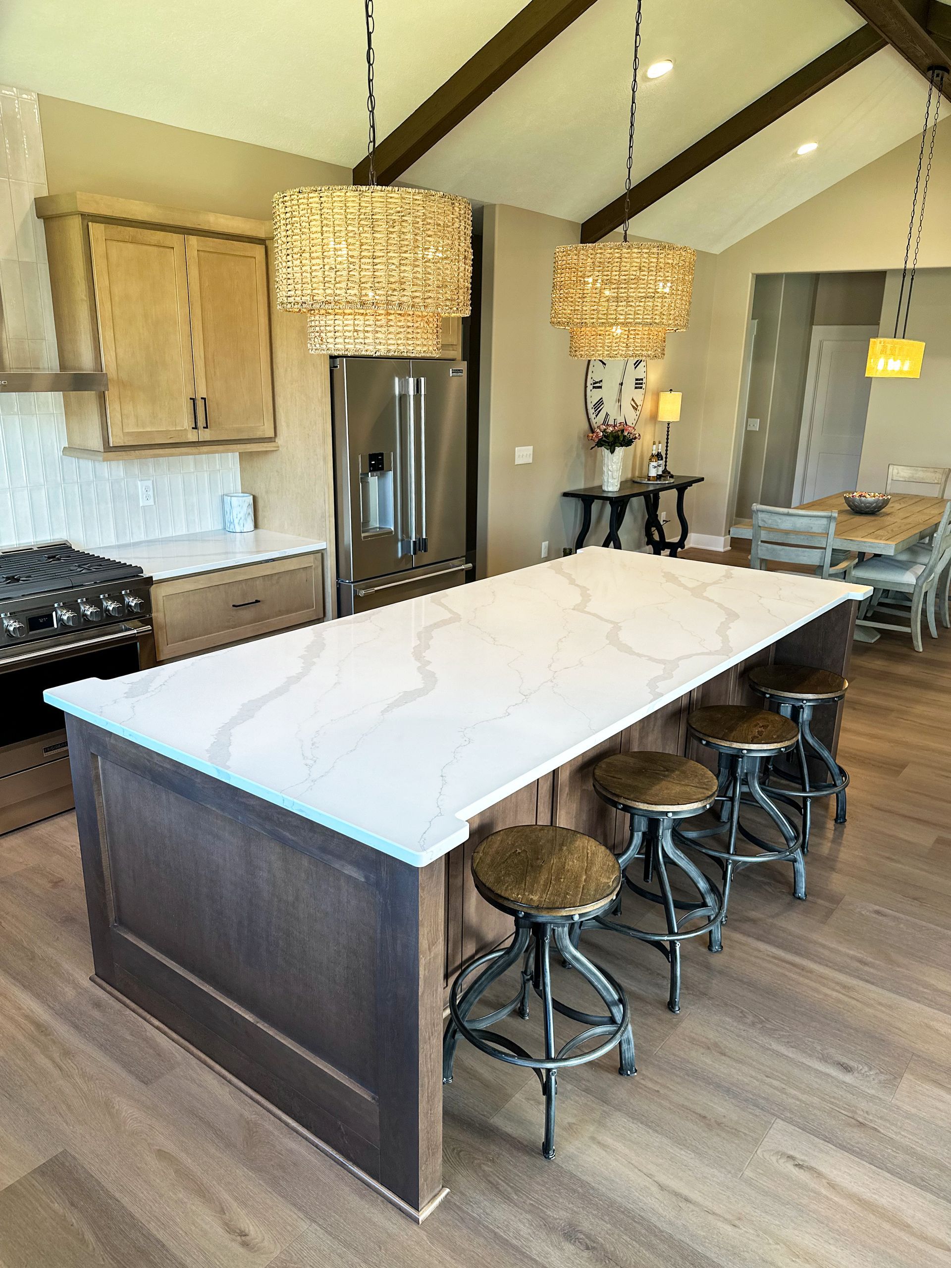 A kitchen with a dark wood island, white quartz countertop, three industrial stools, and two tiered gold pendant lights.