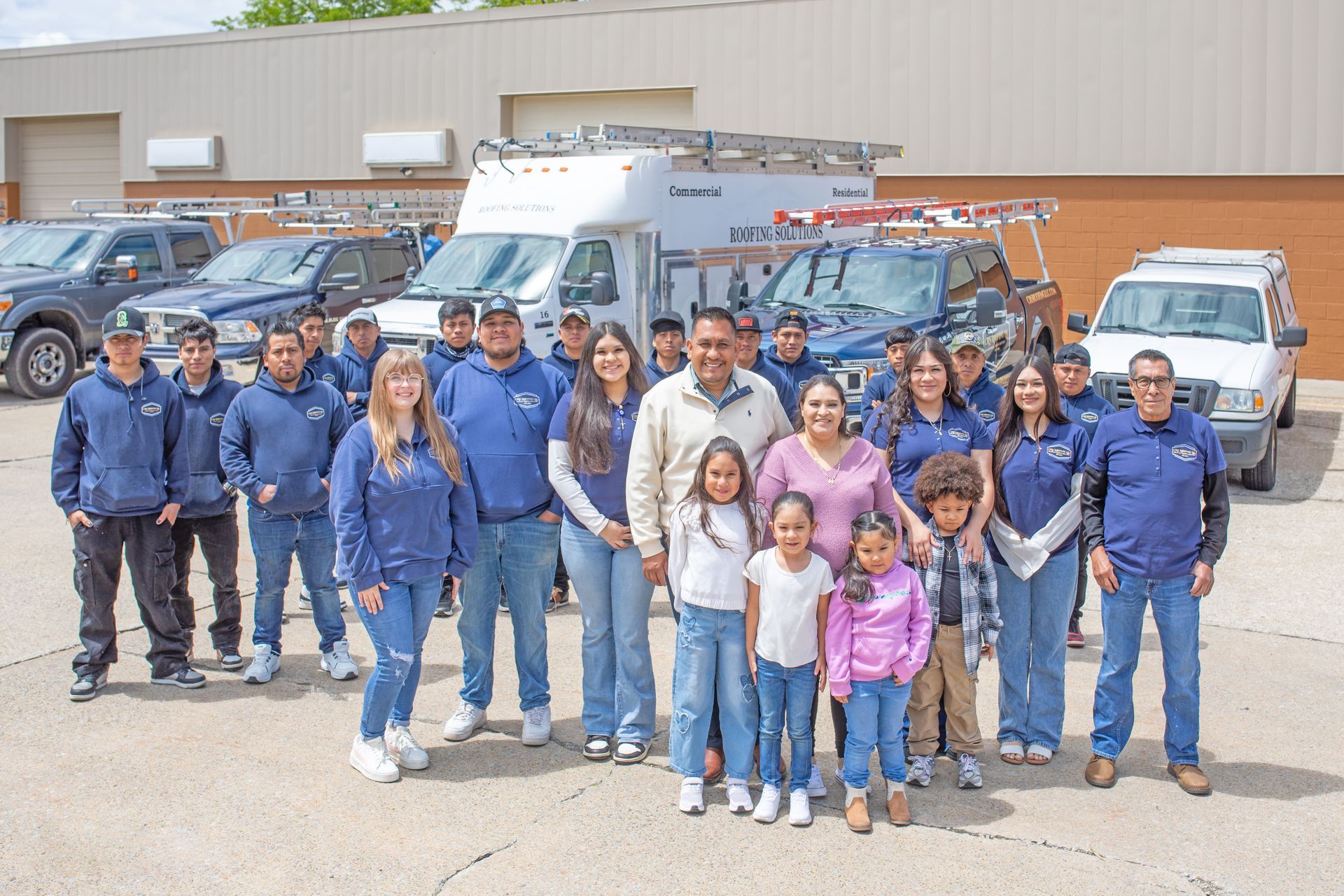 A group of people wearing blue shirts posing in front of work trucks and a large warehouse building.