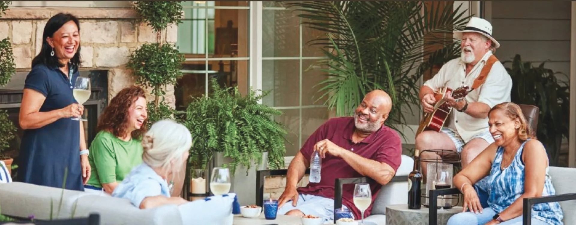 A group of people laughing and socializing on a patio, with one person playing an acoustic guitar.