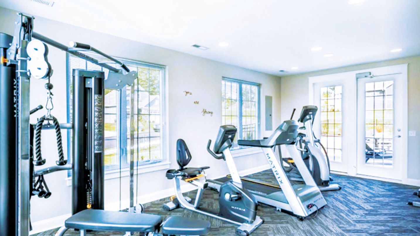 A bright, modern fitness center with a multi-station weight machine, a stationary bike, and two treadmills.