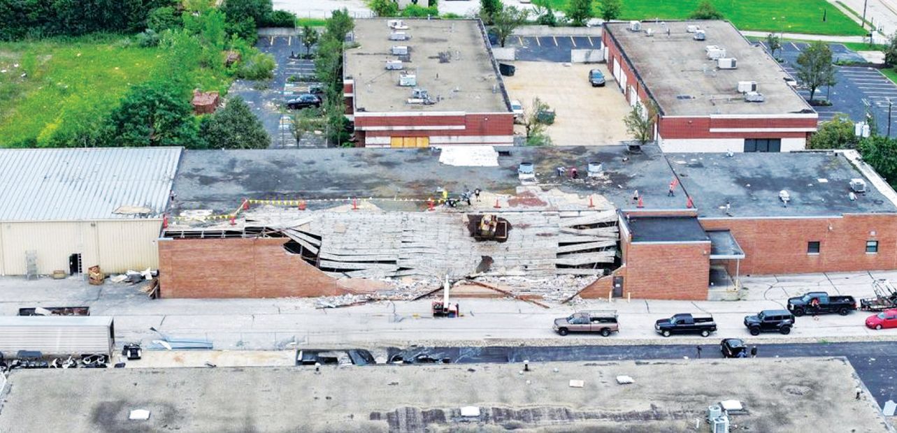 Aerial view of a commercial building with a collapsed roof and caved-in brick wall at the front entrance.
