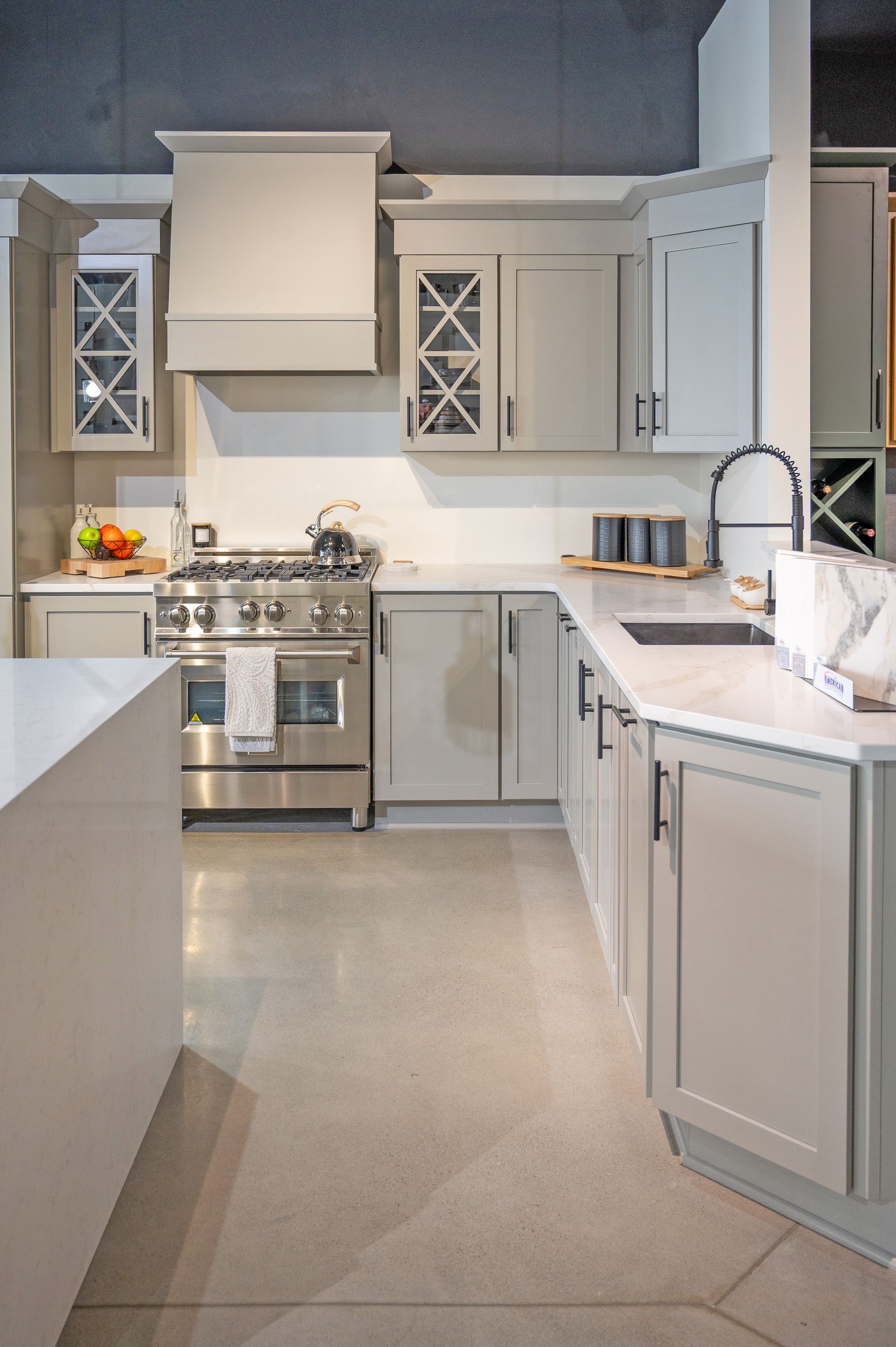 A modern kitchen with light gray cabinets, white countertops, stainless steel appliances, and a central island.