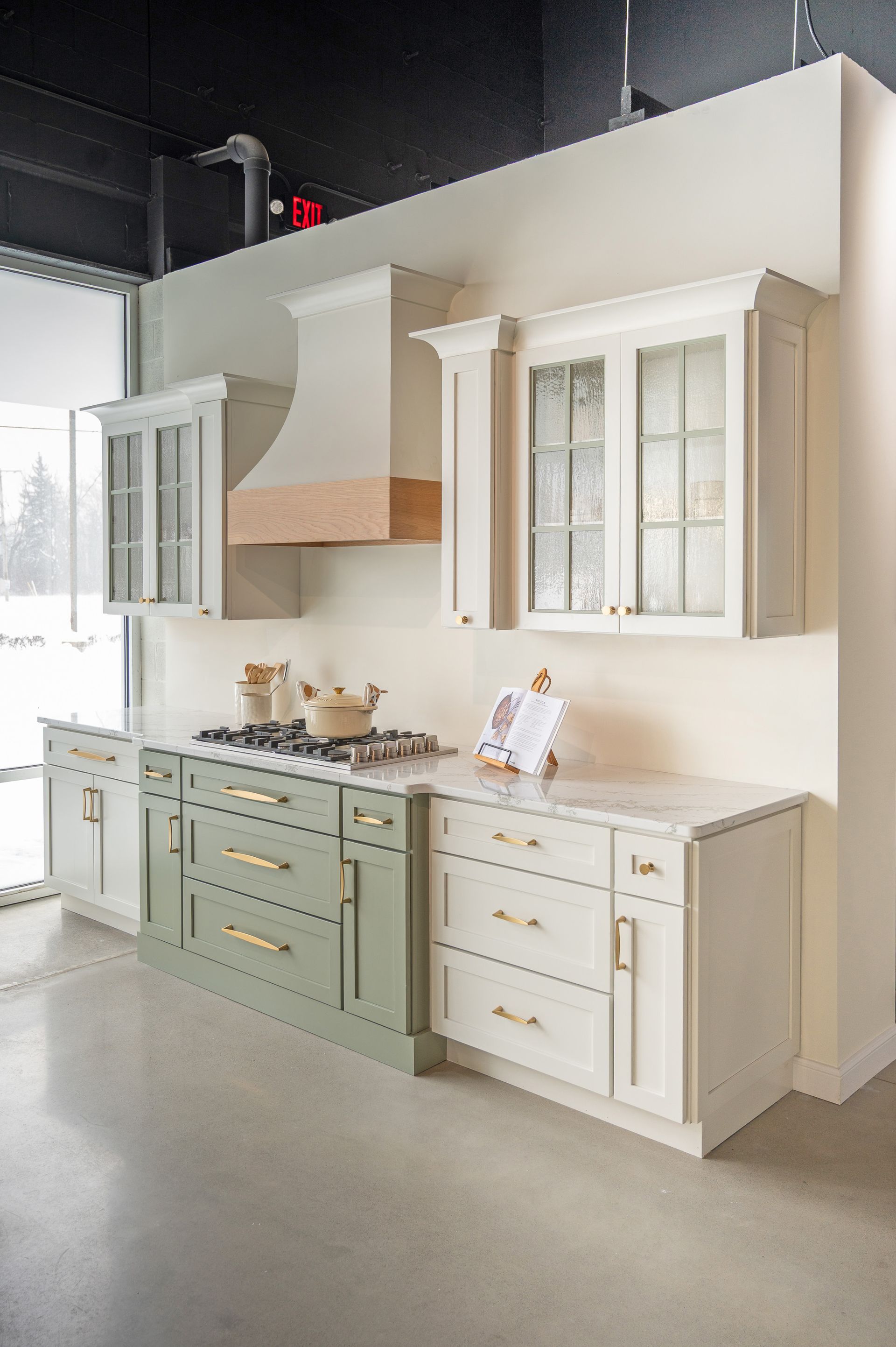Kitchen showroom featuring cream cabinets with glass doors, a green range cabinet, and a matching custom range hood.