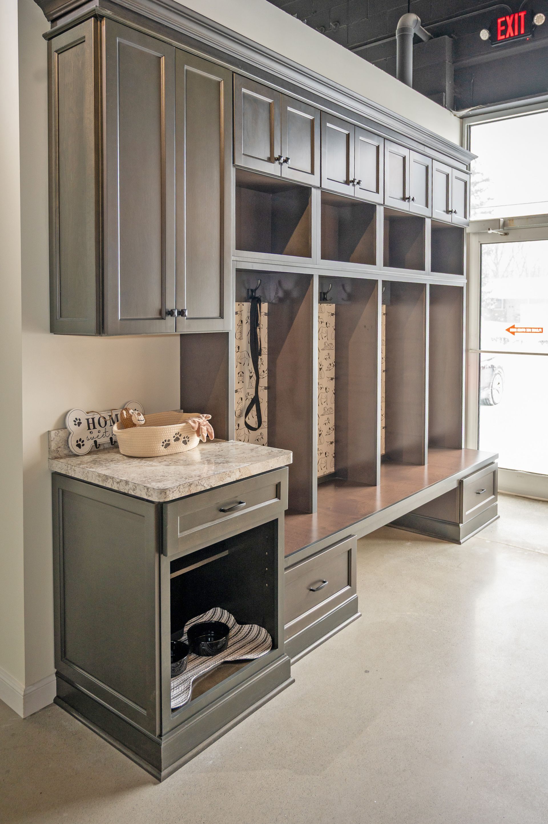 Custom dark gray mudroom storage unit with lockers, countertop, and an integrated pet feeding station in a modern space.