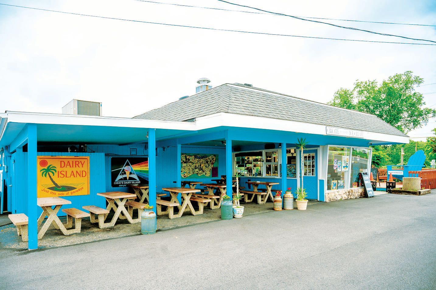 A bright blue Dairy Island ice cream shop with outdoor picnic tables under a covered patio and a shingled roof.