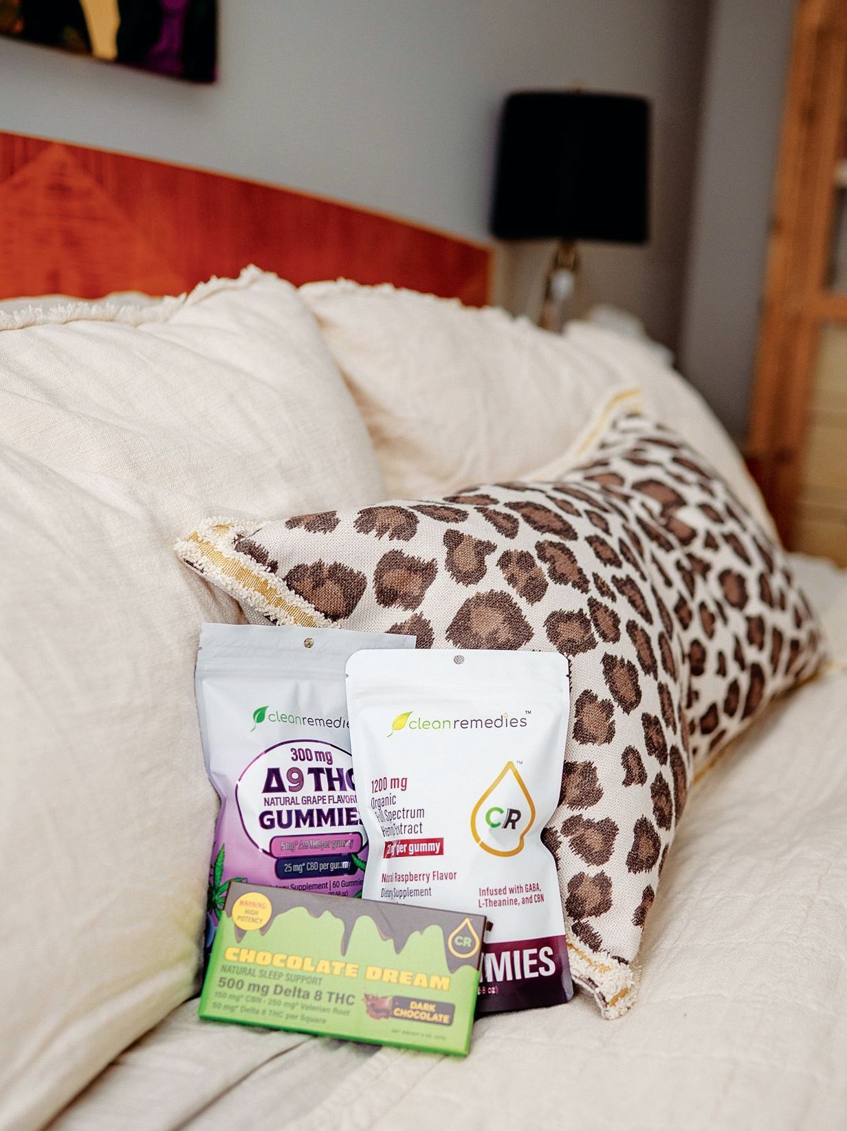 Three packages of cannabis-infused edibles rest against a leopard-print pillow on a bed.