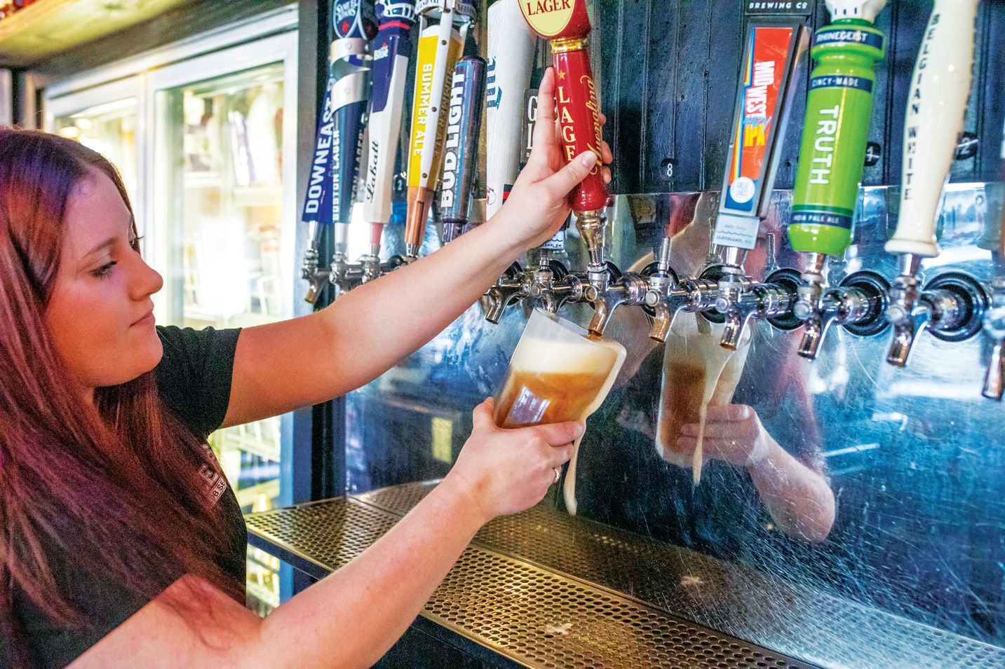 A person pours a beer from a draft tap handle into a glass at a bar.