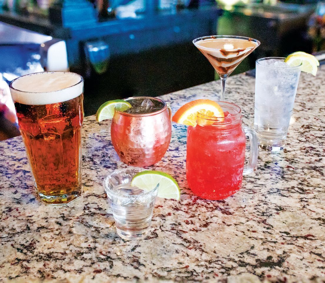 A selection of assorted cocktails and a beer on a granite bar top, featuring a variety of glassware and garnishes.