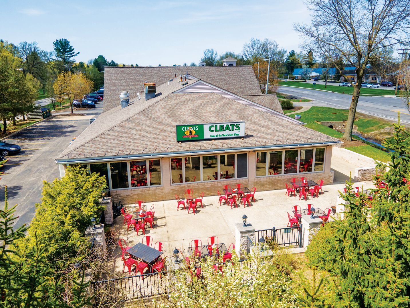 An elevated view of a restaurant with a beige stone exterior, tan roof, and outdoor patio with red tables and chairs.