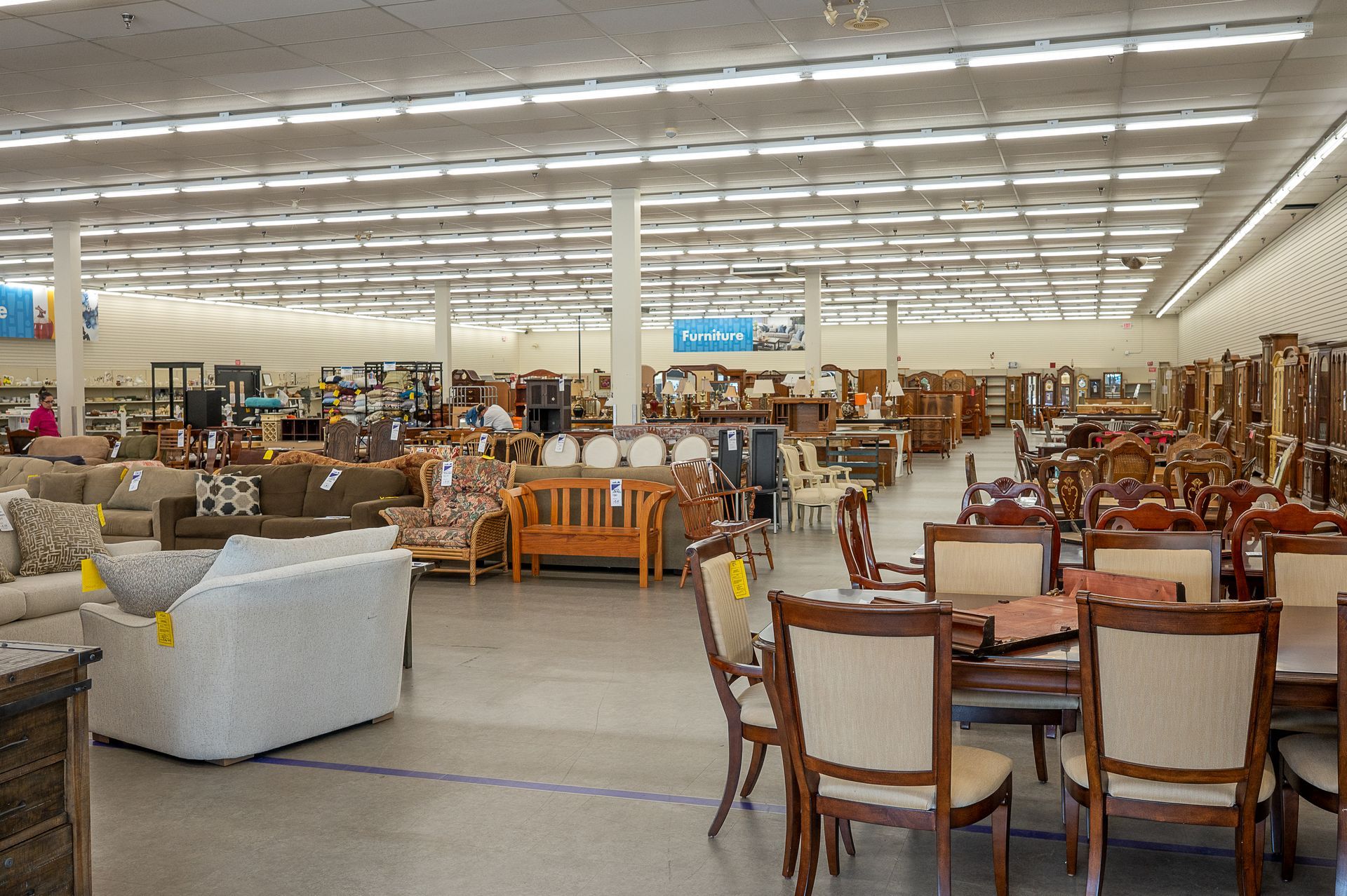 A spacious furniture showroom filled with various dining sets, sofas, and armchairs arranged under bright lighting.