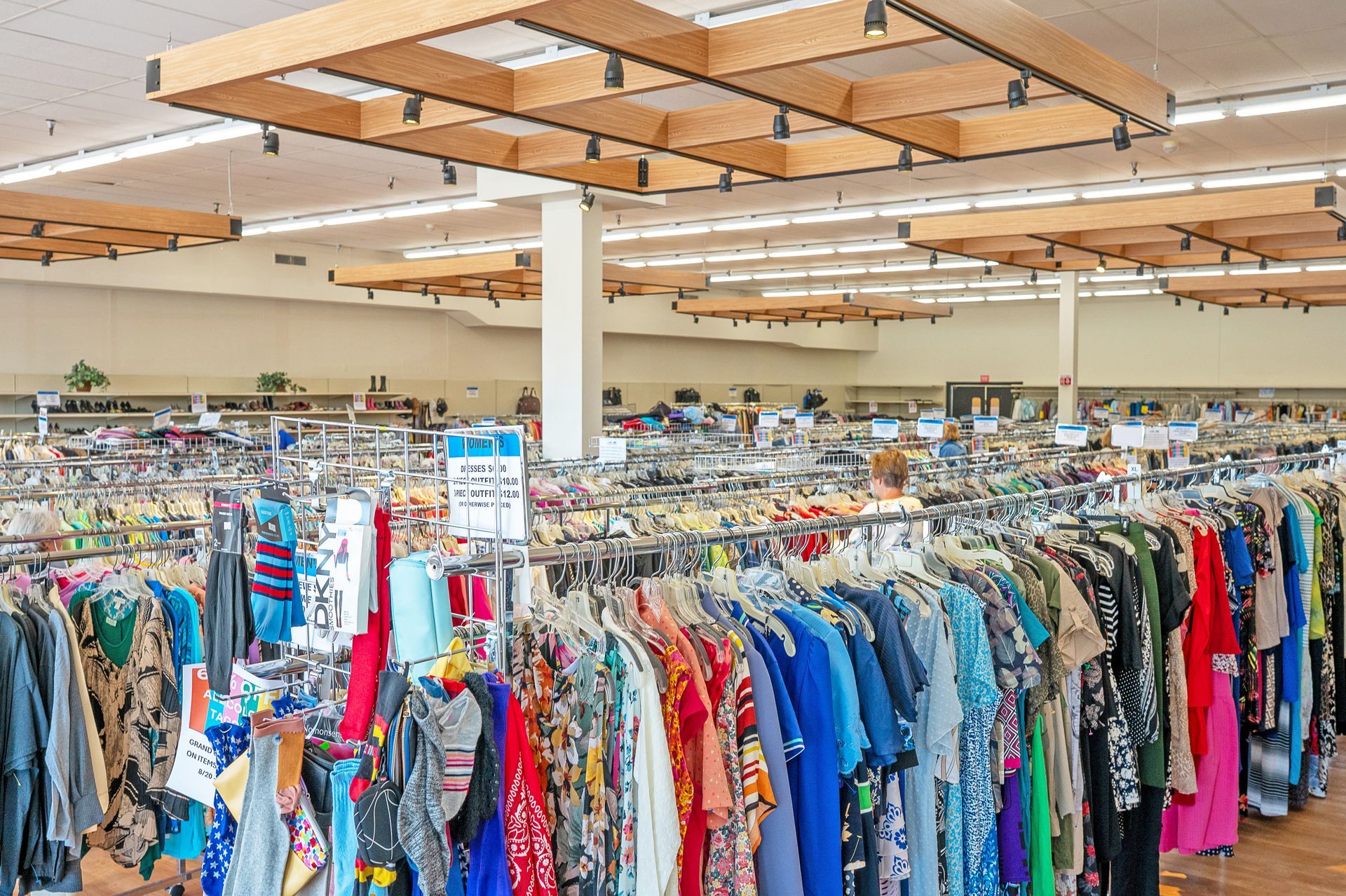Clothing racks filled with various garments in a large, brightly lit indoor retail store with wooden ceiling fixtures.