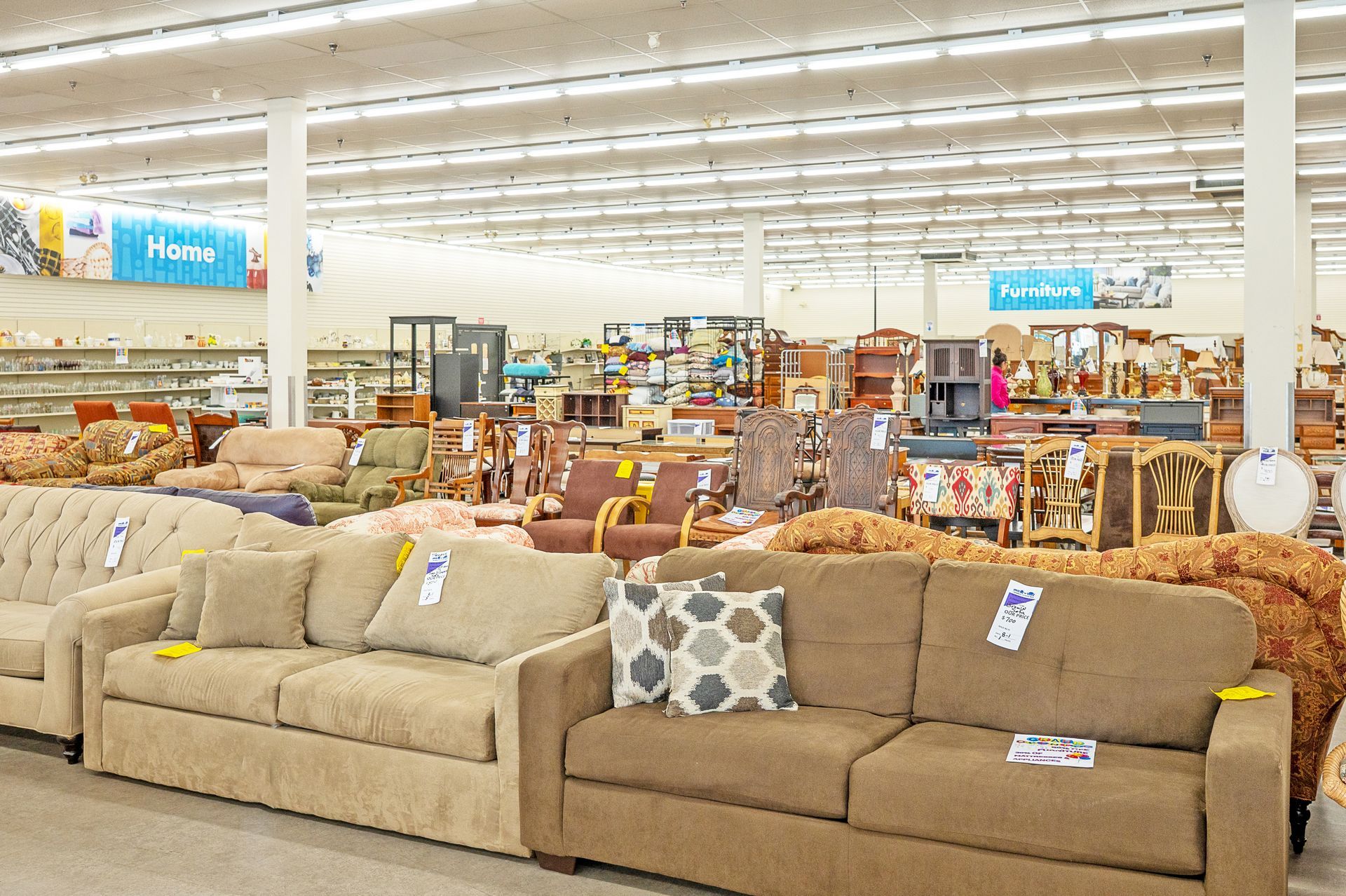A wide view of a furniture store showroom floor featuring multiple fabric sofas and chairs with price tags attached.