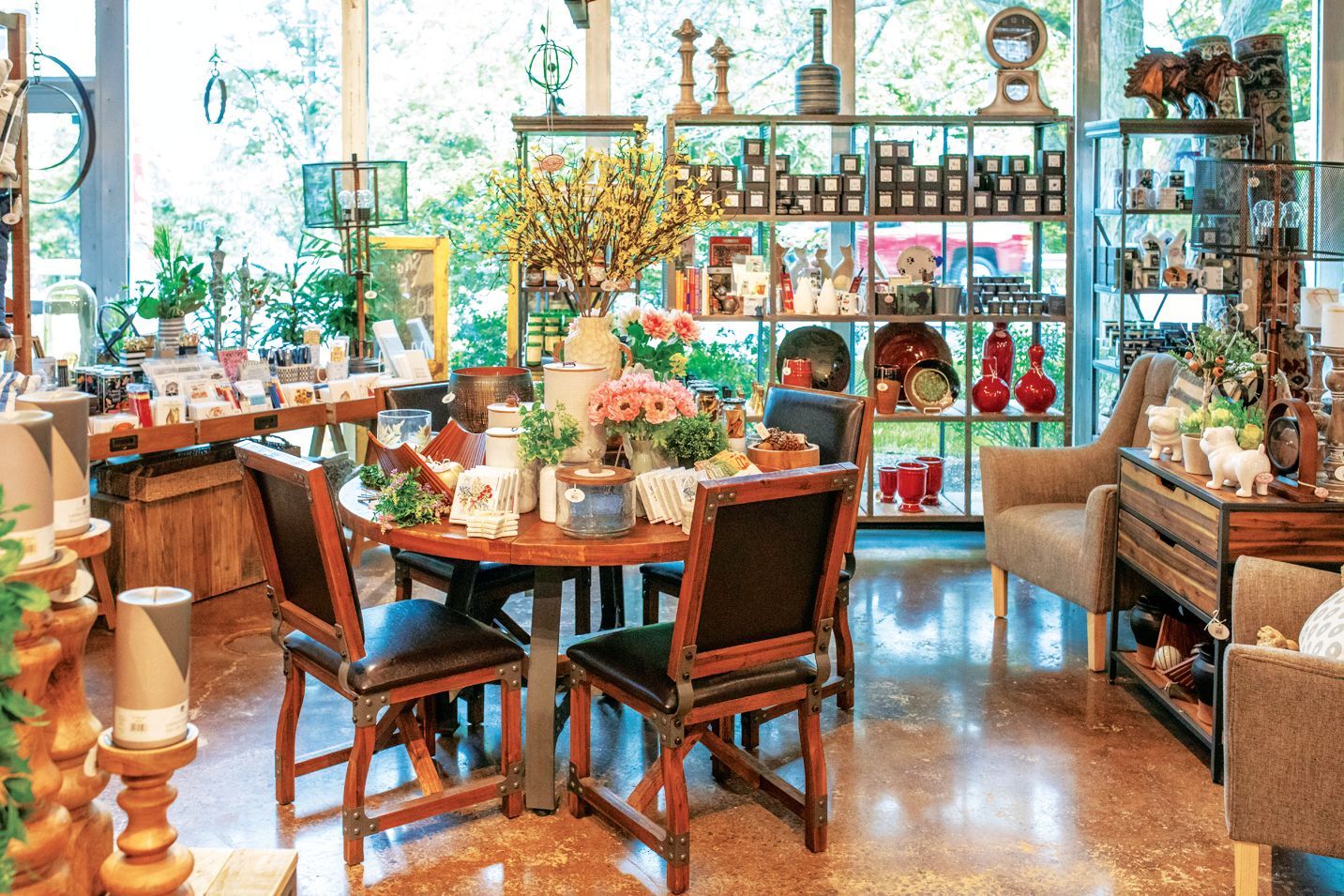 A brightly lit home decor shop features a wooden dining set surrounded by shelves filled with various home accessories.