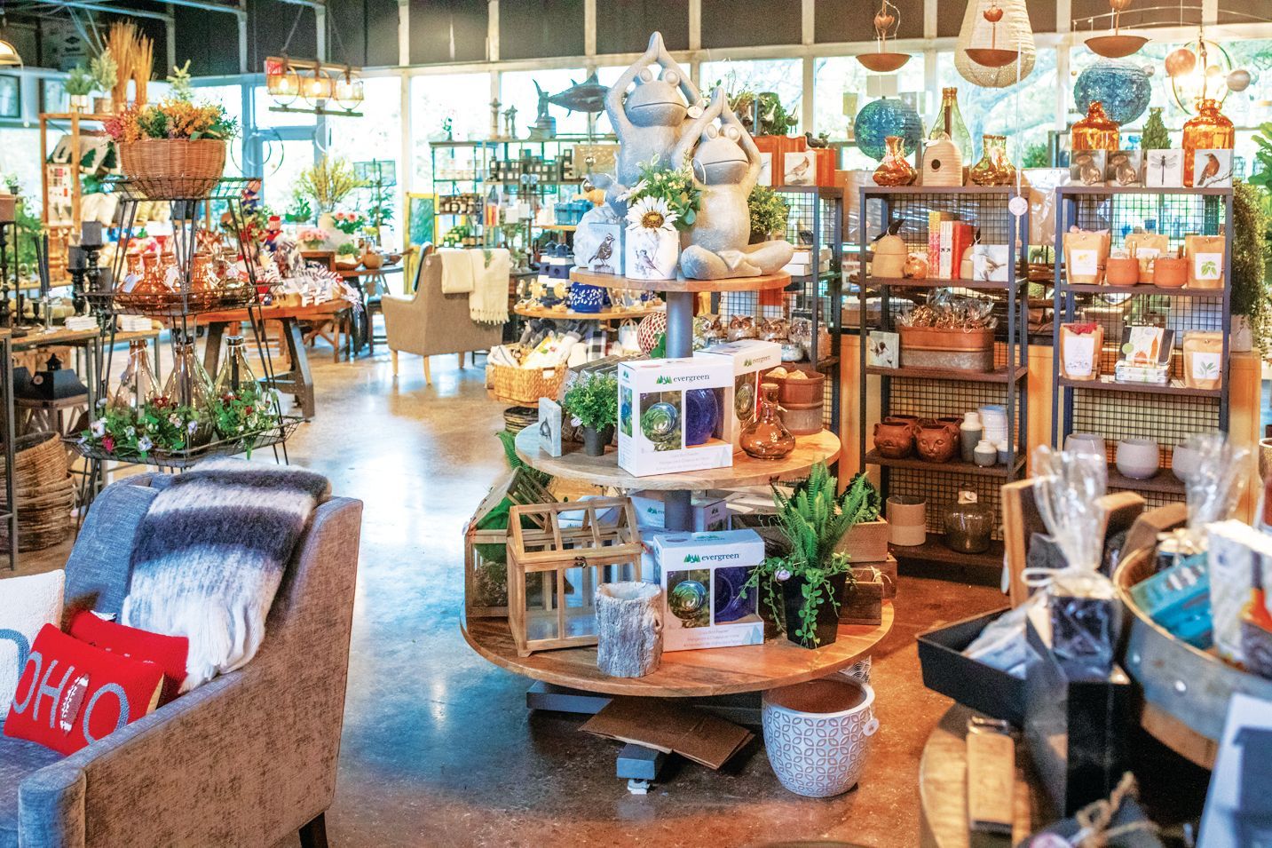 A shop interior filled with home decor, including a central display stand, shelves of items, and a comfortable armchair.