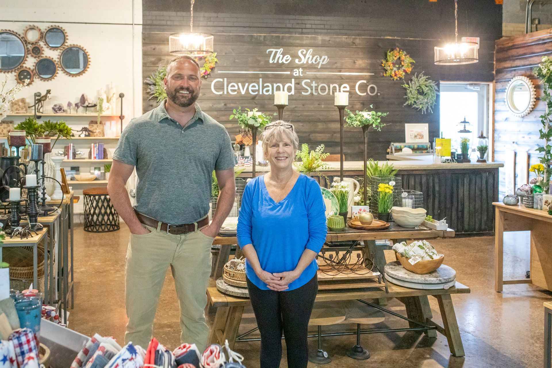 A man and woman stand in The Shop at Cleveland Stone Co., a retail store featuring rustic decor and stone accents.