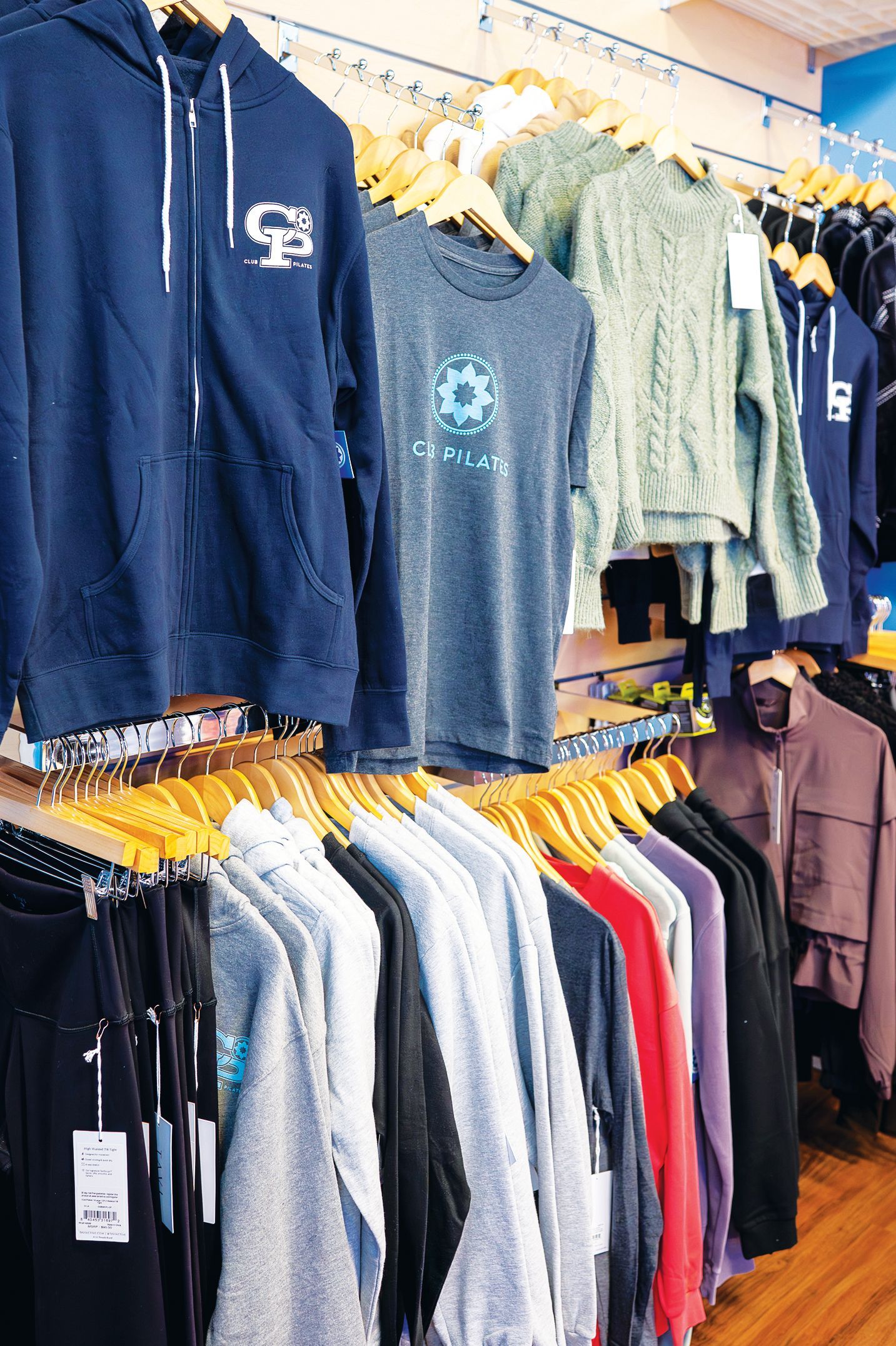 Clothing store racks filled with hanging hoodies, t-shirts, and sweaters in various colors, organized on wooden hangers.