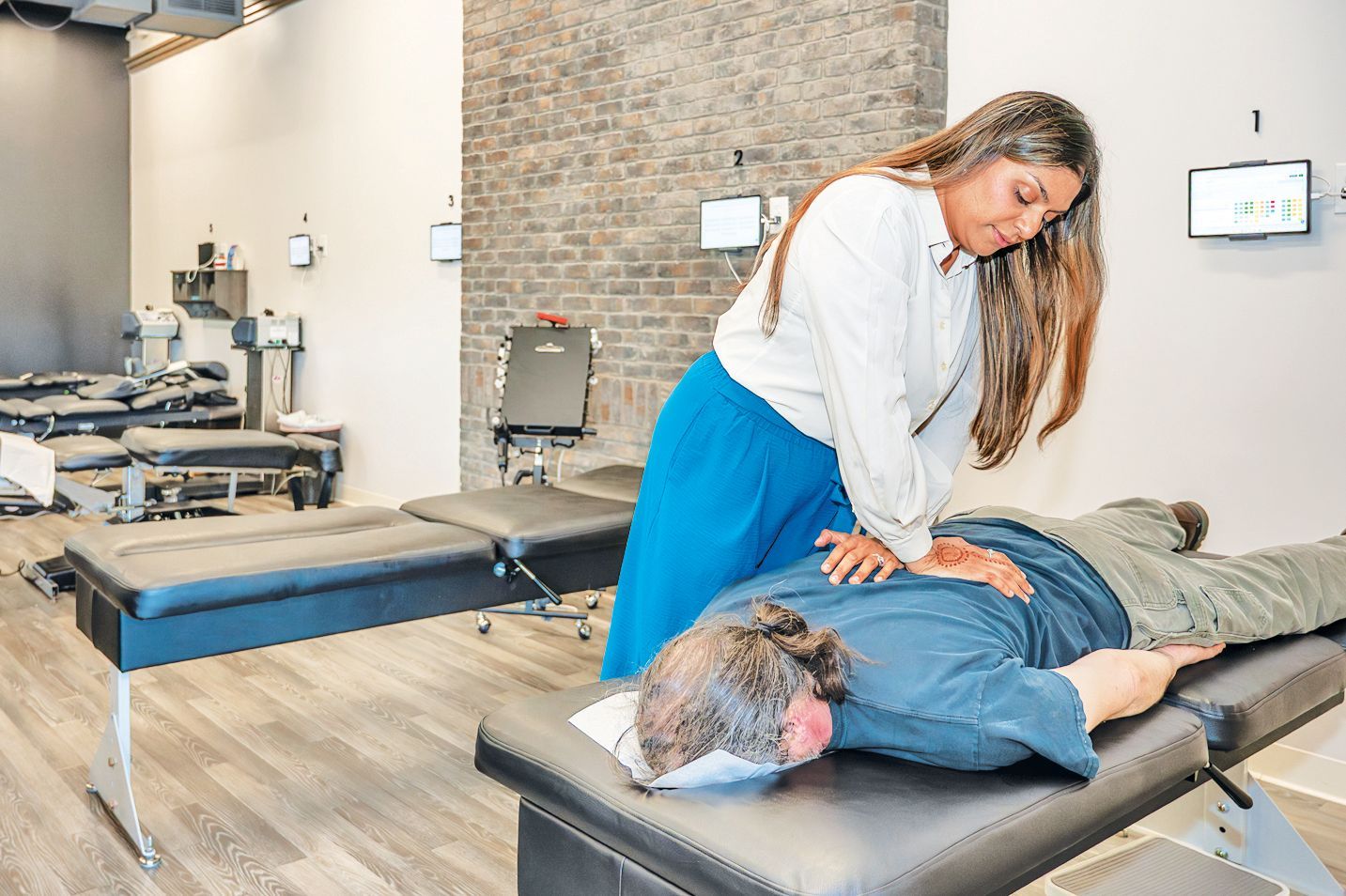 A chiropractor performs a spinal adjustment on a patient lying prone on a treatment table in a modern clinic.