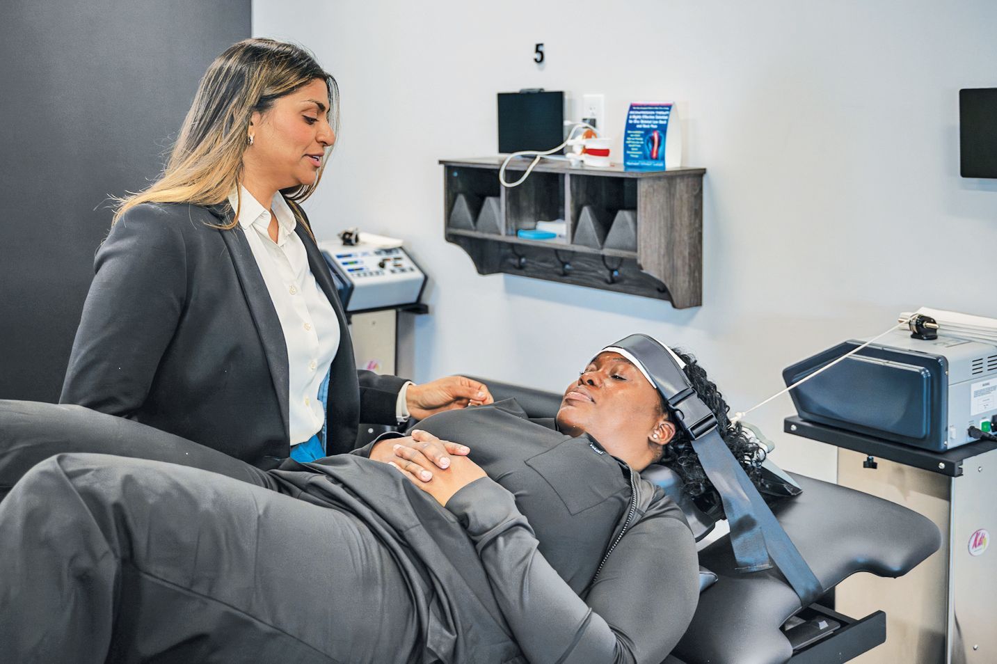 A medical professional standing next to a patient lying on a table wearing a TMS treatment head coil device.