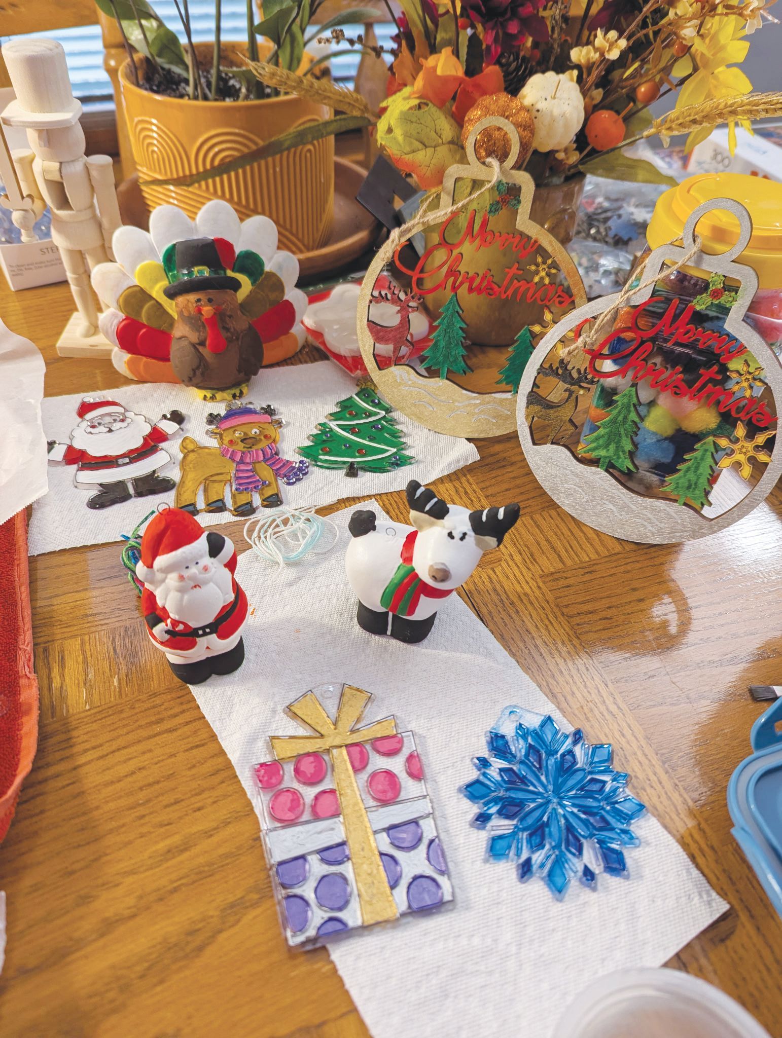 Craft supplies, including ornaments, felt cutouts of Santa and a turkey, and painted decorations on a wooden table.
