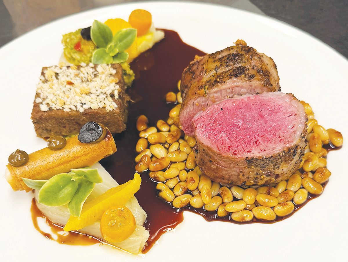 Plated medium-rare pork tenderloin with brown sauce, a bean garnish, vegetable slices, and a topped savory square.