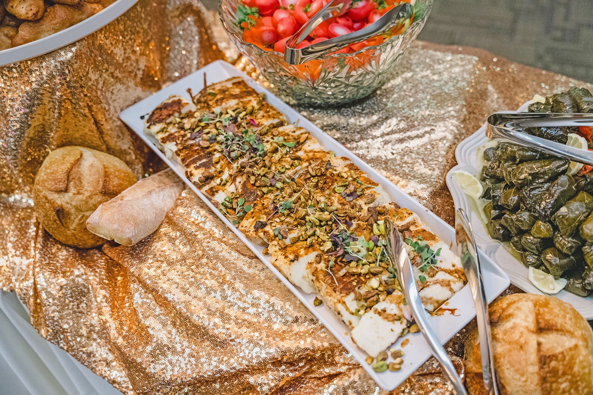 A high-angle view of a buffet spread featuring a central platter of grilled fish, bread, grape leaves, and a salad.