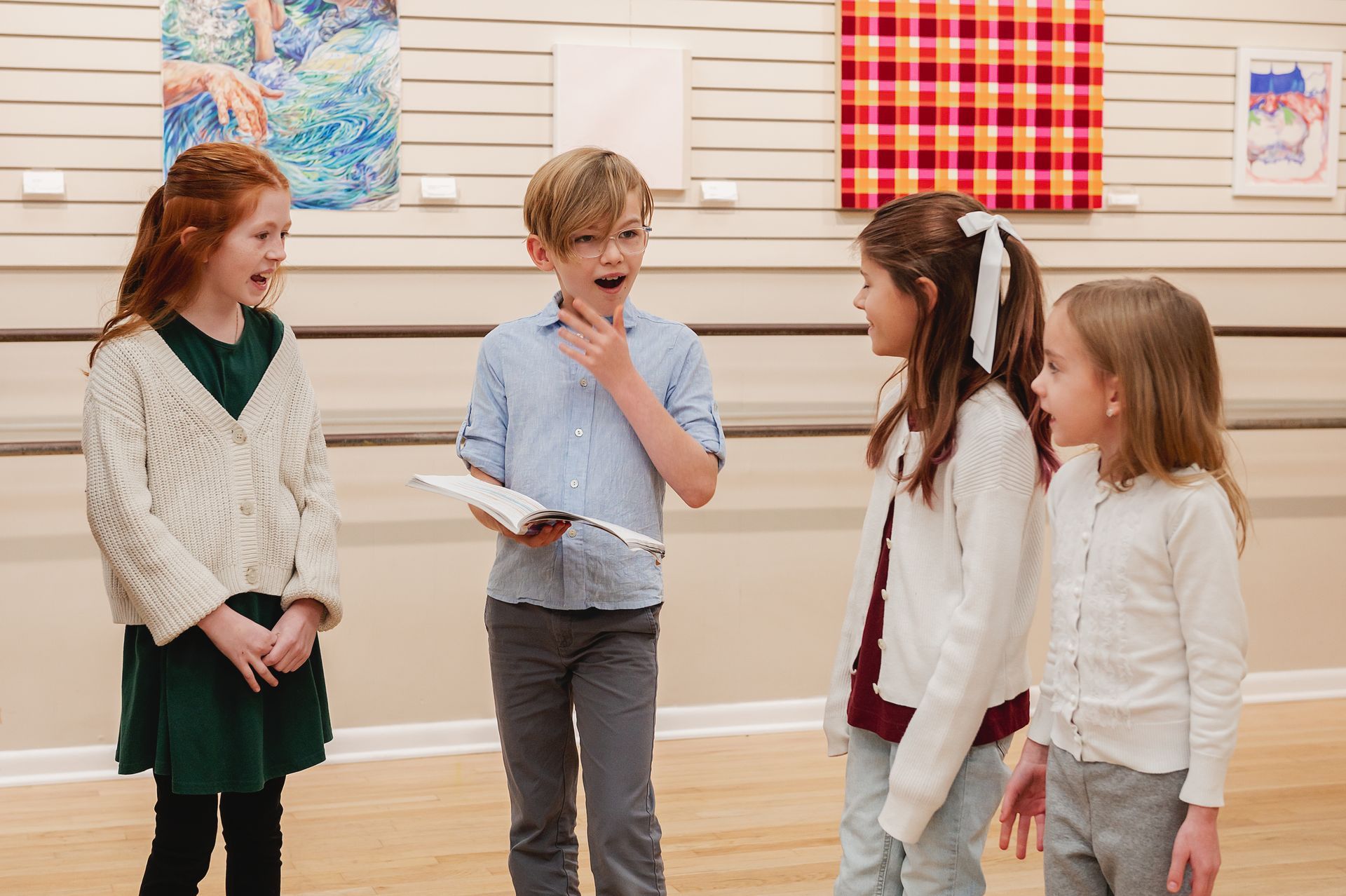 Four children stand in an art gallery, engaged in conversation while observing artworks displayed on the wall.
