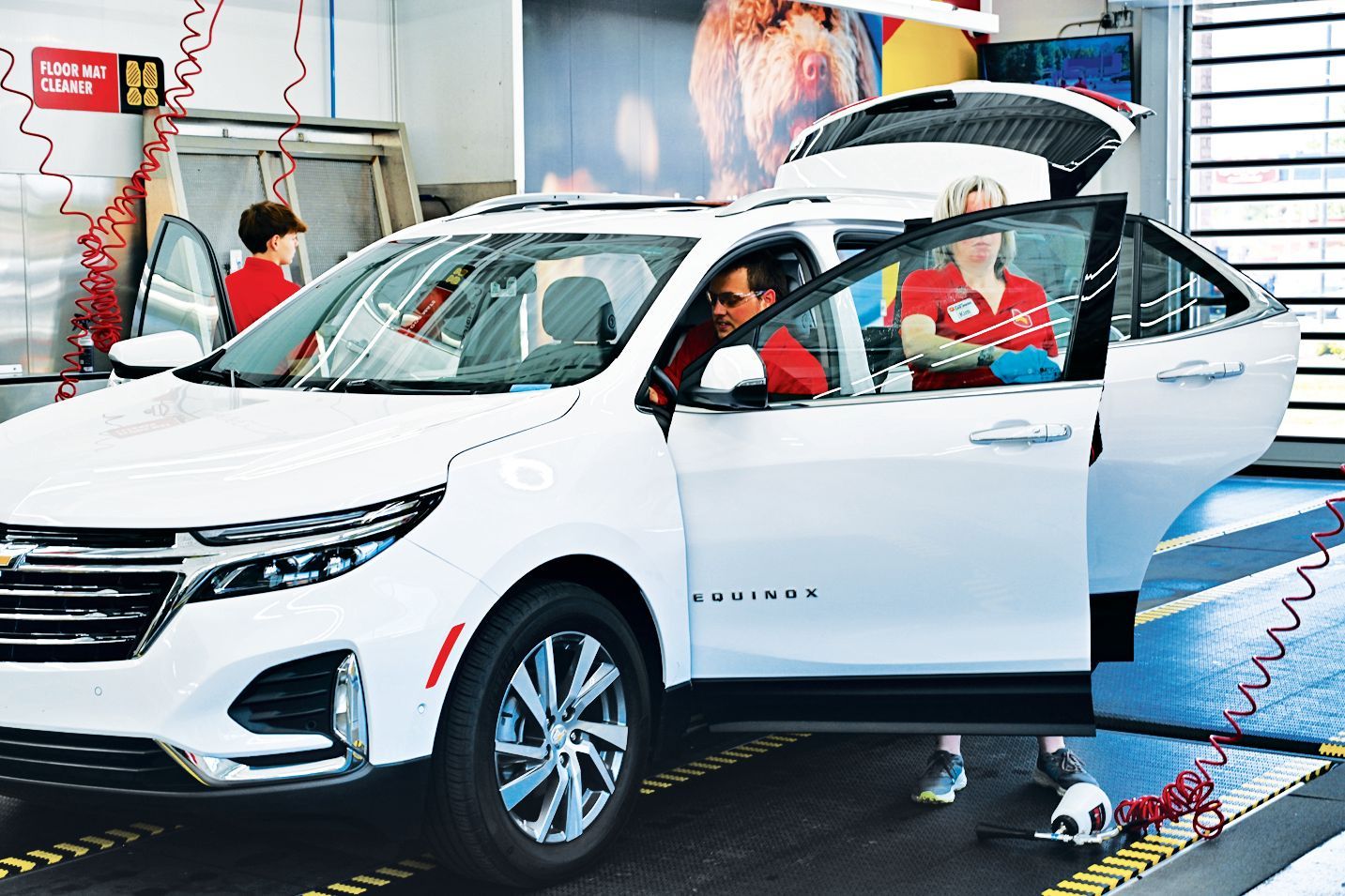 A white Chevrolet Equinox in a service garage with open doors and a technician working inside.
