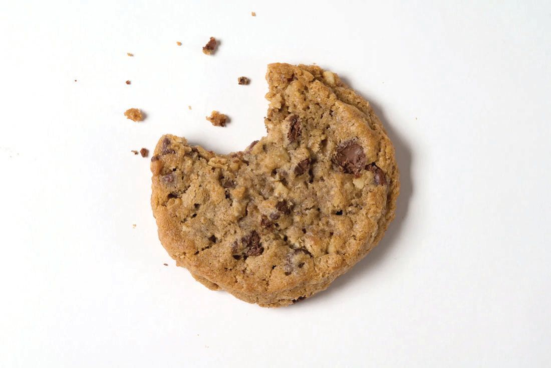 A partially eaten chocolate chip cookie with scattered crumbs against a white background.