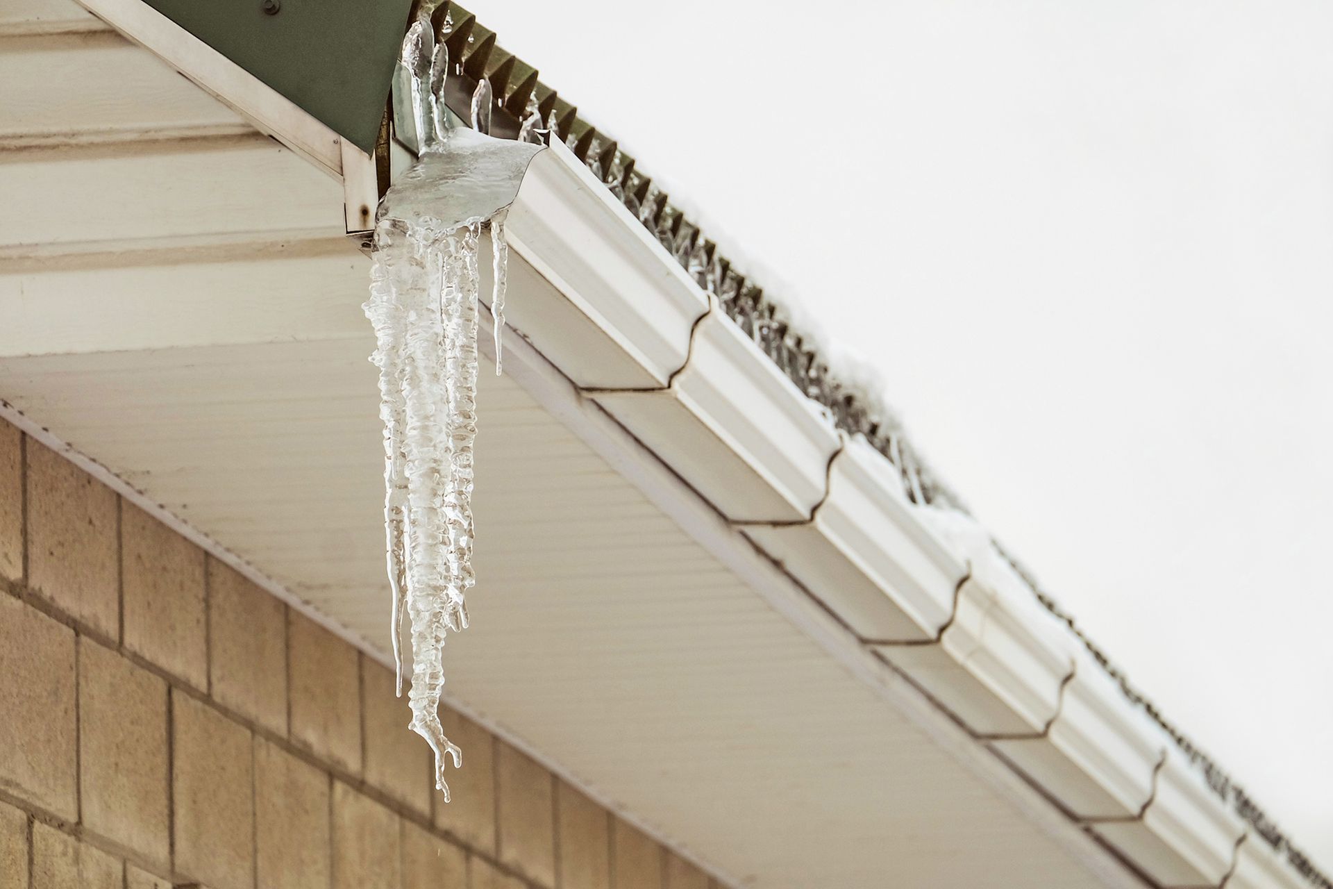 Icicles hanging from the white gutter of a residential building on a cloudy winter day.