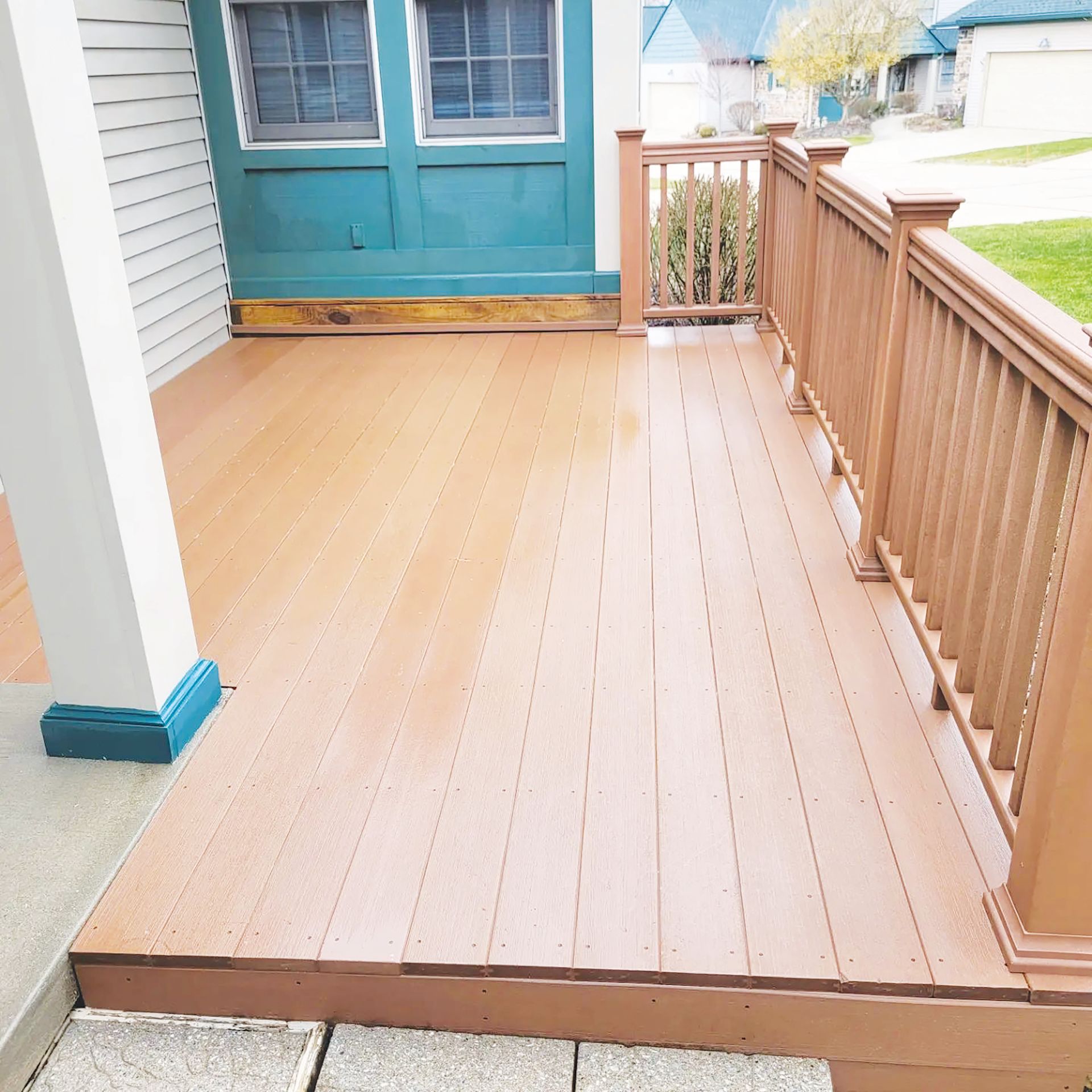A freshly painted wooden deck with a brown railing, located outside a house with blue window trim and white siding.