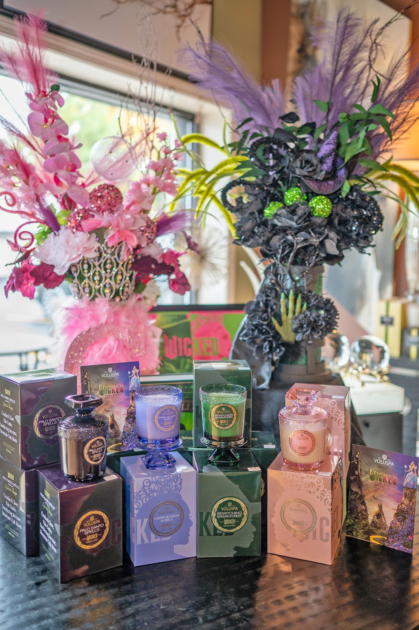 Arrangement of assorted boxed candles displayed below colorful floral bouquets, including a themed Halloween arrangement.