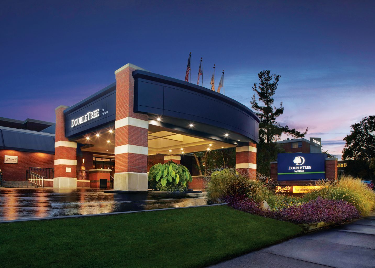 The entrance of a DoubleTree hotel at twilight, featuring a brick-columned porte-cochere and a landscaped lawn.