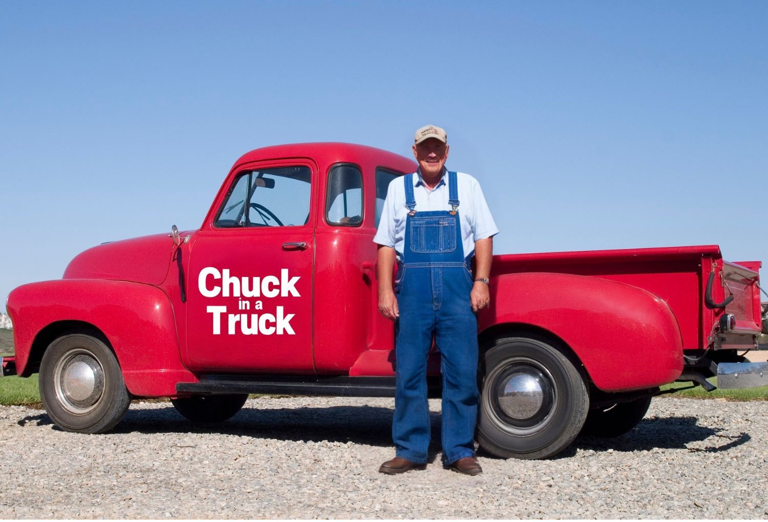 A person in a light blue shirt and blue overalls stands in front of a red vintage pickup truck labeled