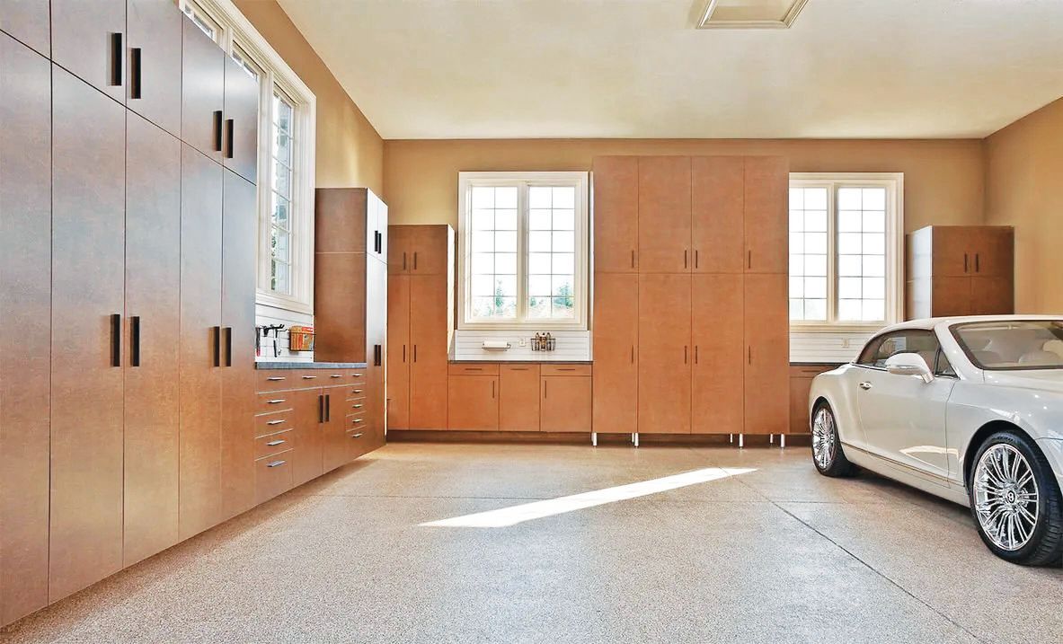 A bright garage with light wood cabinetry, speckled floors, and a silver sports car parked on the right.