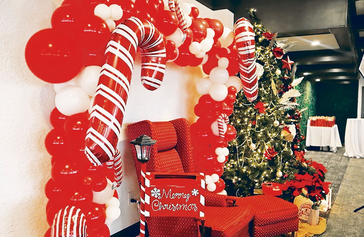 A Christmas-themed setup with red balloons, two candy cane props, a Santa-style chair, and a decorated tree.