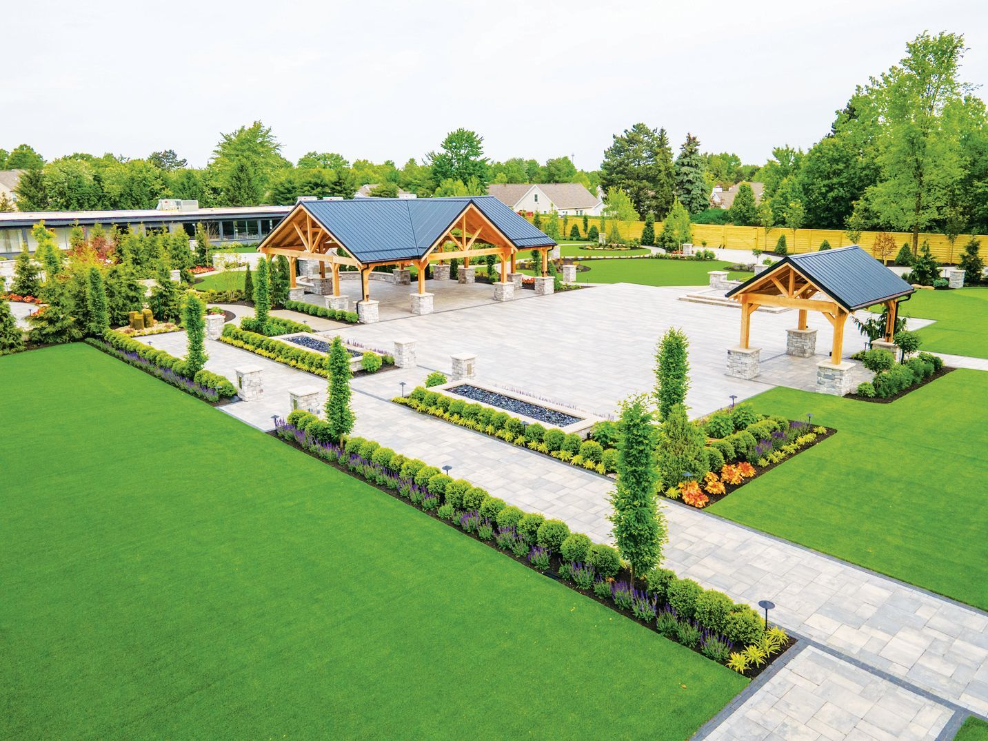 An aerial view of a manicured park with stone walkways, trimmed hedges, a large pavilion, and a smaller gazebo.
